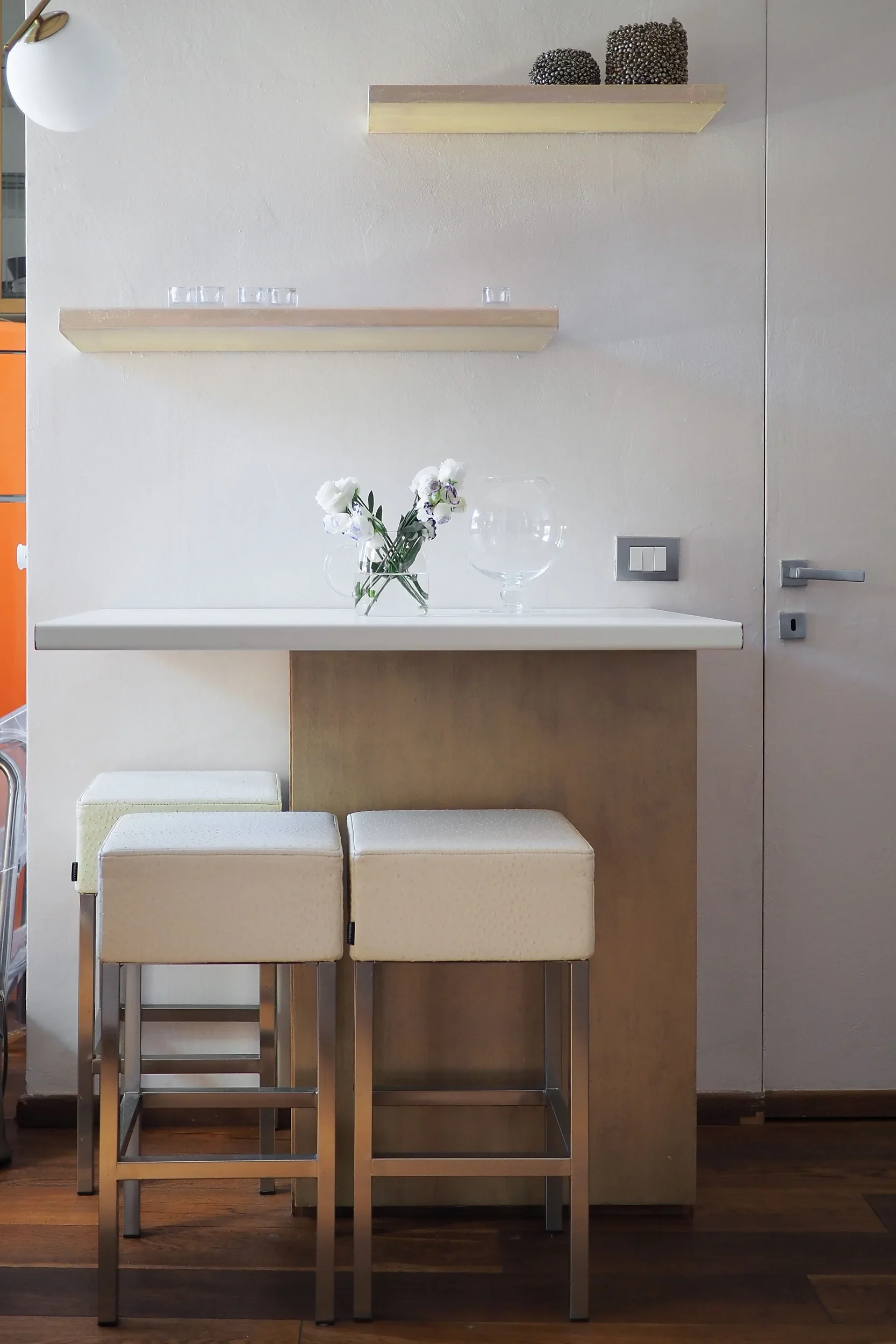 White dining counter with two stools, wall shelves and white flowers