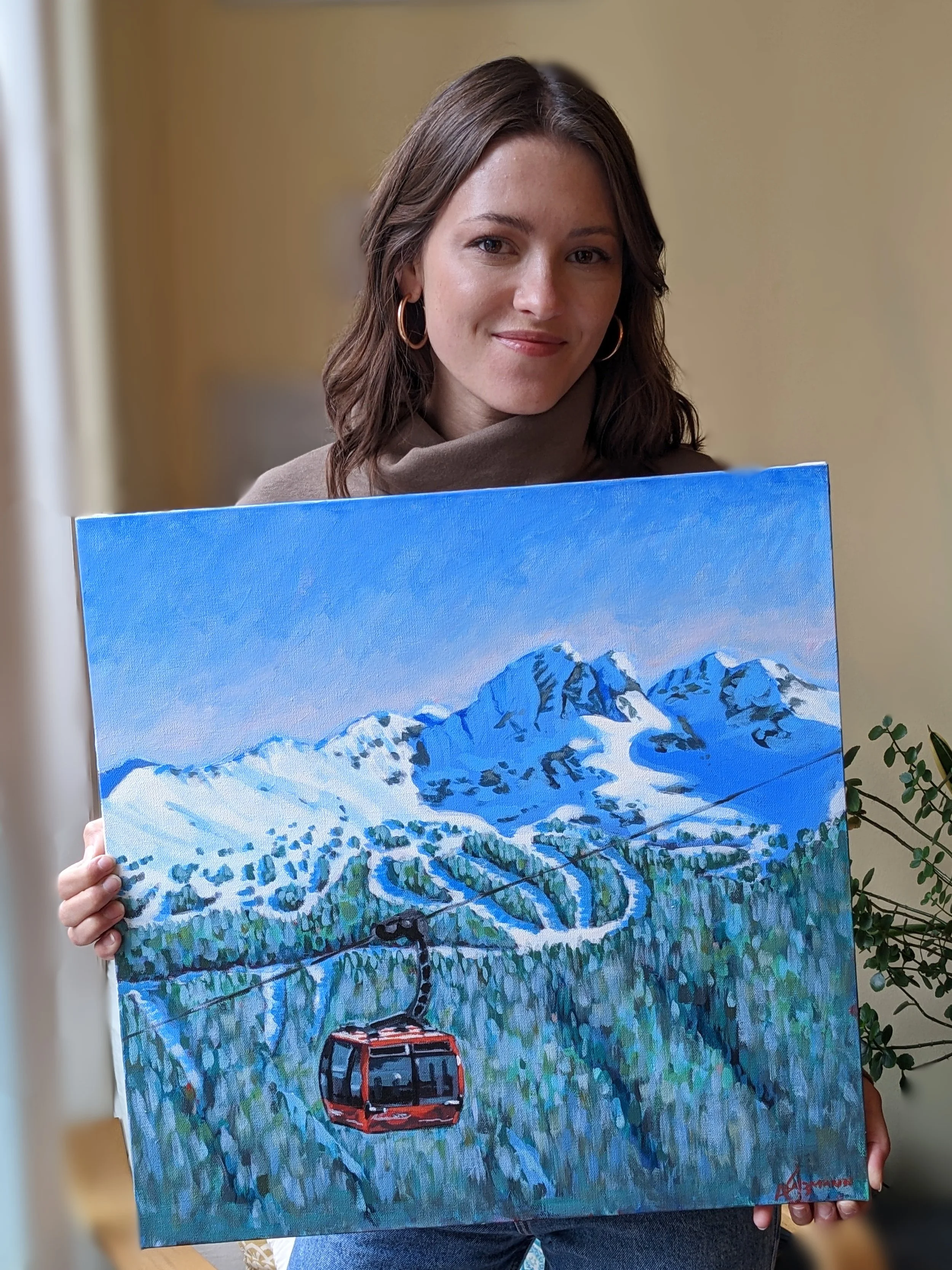A woman holding a colorful painting of mountain scenery with a ski lift and winding ski trail.