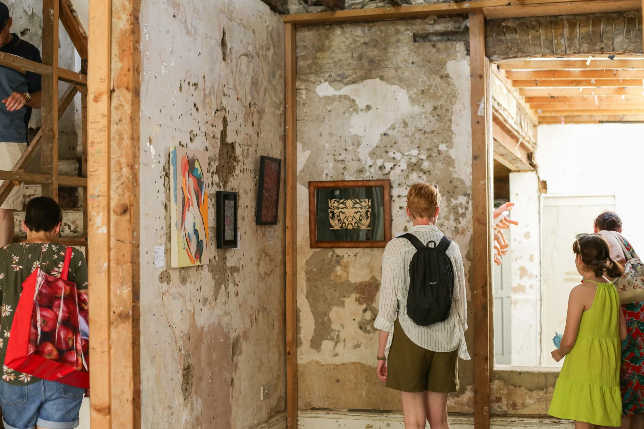 People viewing artwork in a gallery with unfinished stone walls and wooden framing.