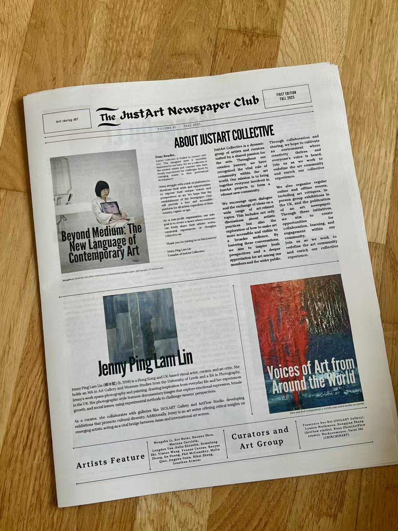 A newspaper titled 'The JustArt Newspaper Club' lying on a wooden surface. The front page features a black and white photo of a woman with short hair holding a laptop, headlines about contemporary art and featured artists, and articles about art projects and exhibitions.