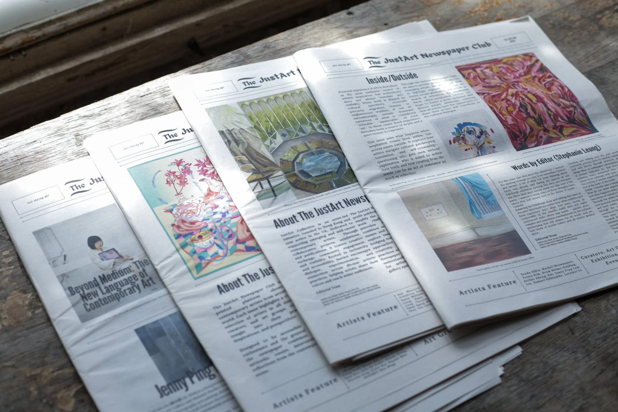 Open newspaper titled 'The JustArt Newspaper Club' spread out on a wooden surface. The page features colorful artwork, articles, and images related to contemporary art and artists.