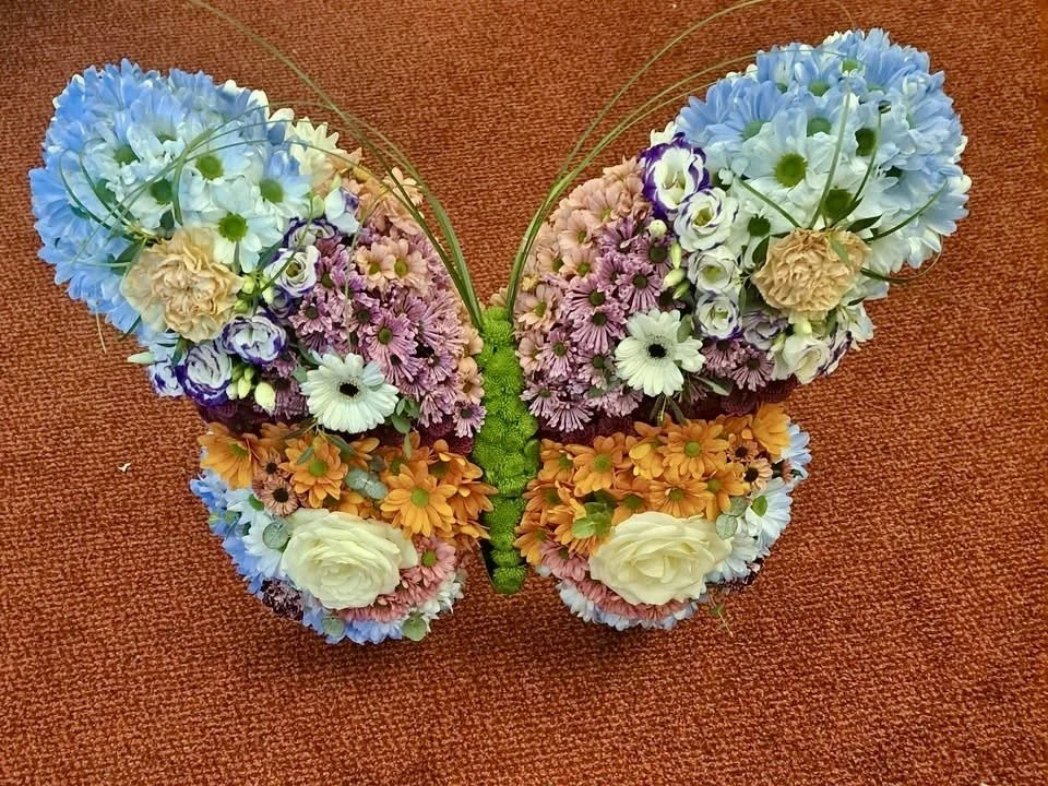 A butterfly-shaped arrangement of colorful flowers on a brown textured surface.