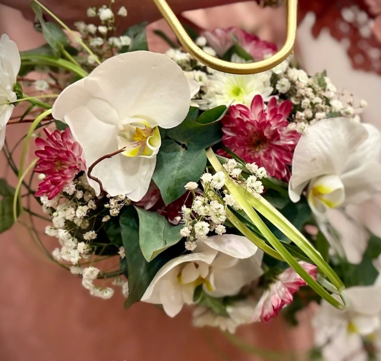 Close-up of a bouquet with white orchids, pink dahlias, baby's breath, and greenery.
