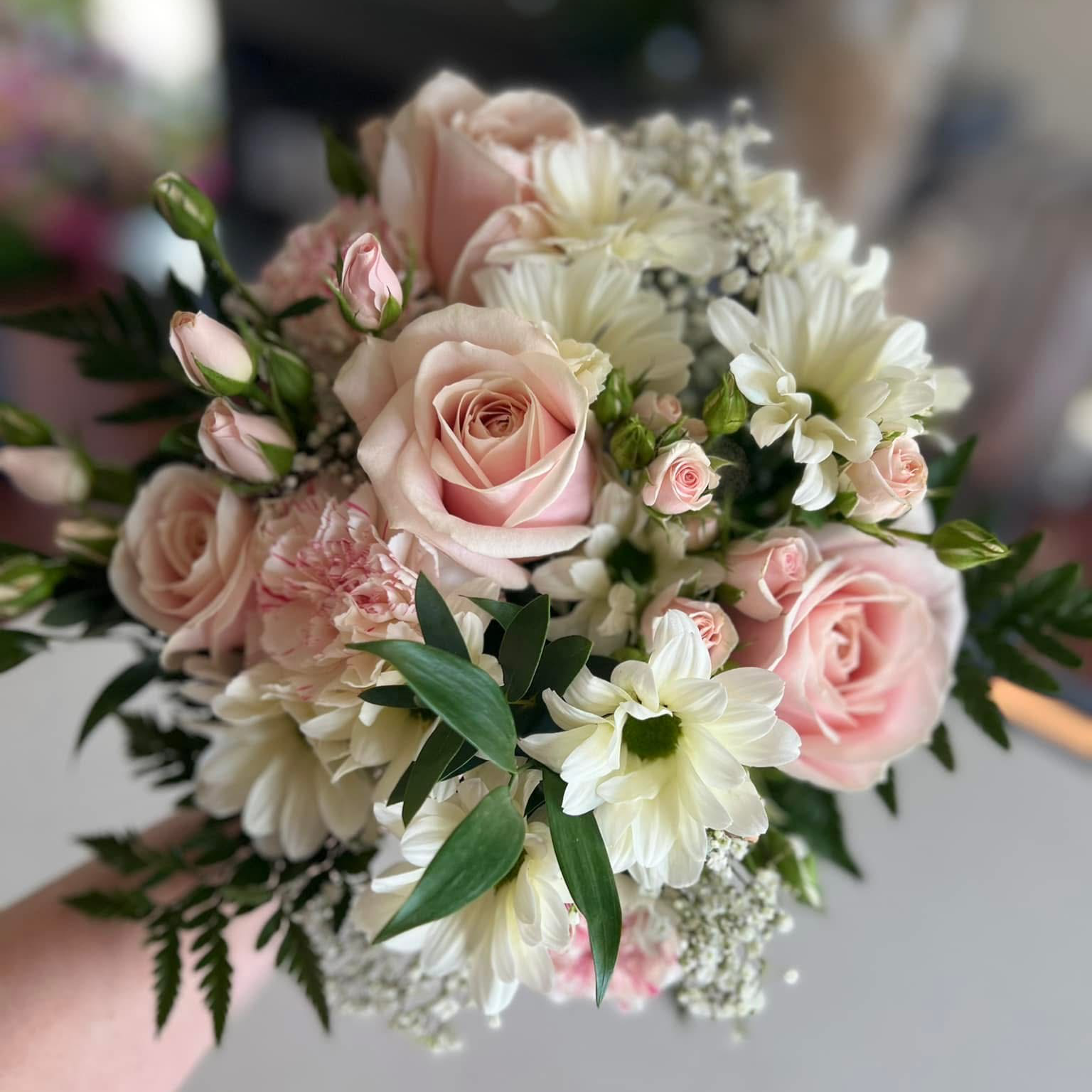 A bouquet of pink roses, white daisies, baby's breath, and greenery.