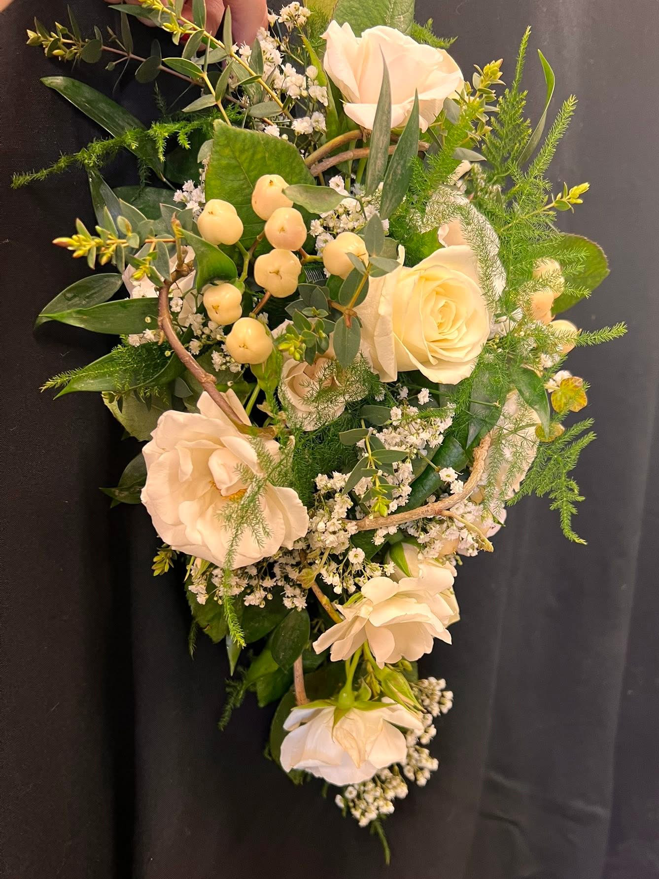 A floral arrangement with white roses, green leaves, and small white filler flowers on a black background.