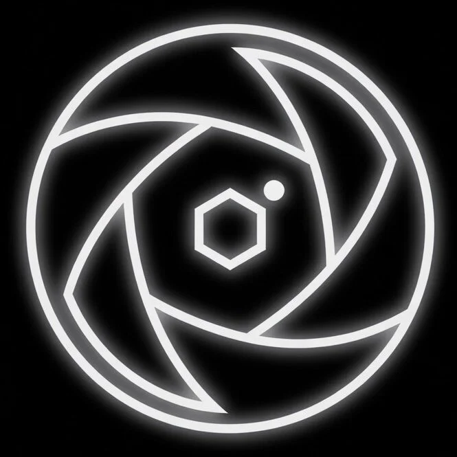 Neon sign with a circular geometric design composed of interconnected lines and shapes, including a hexagon and a small circle, on a black background.