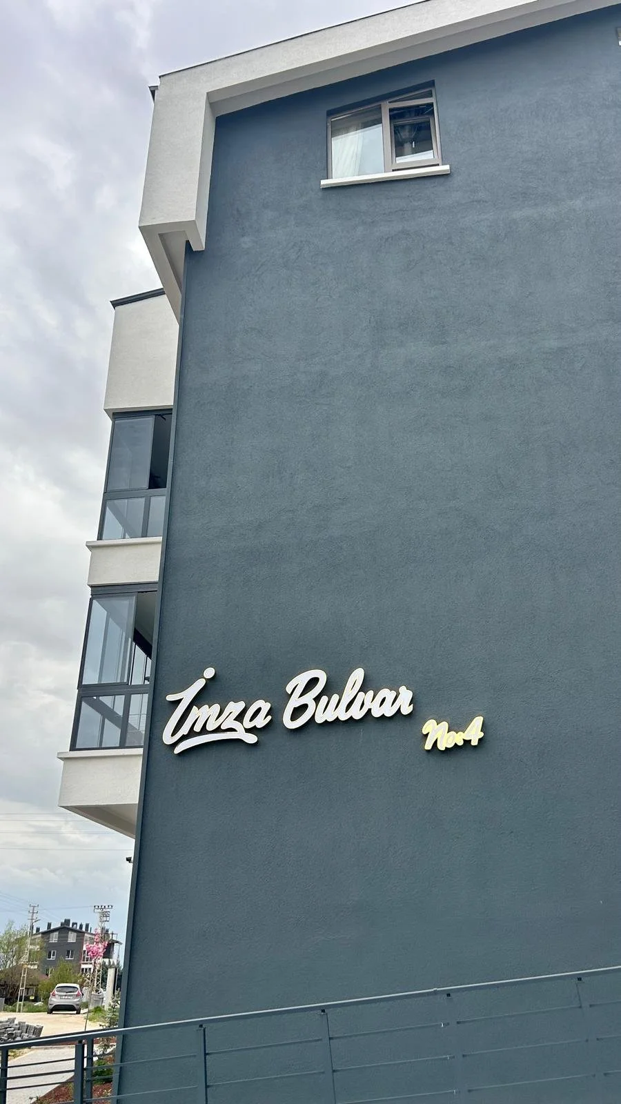 Apartment building with a blue exterior wall and white sign that reads 'İmza Bulvar No 4', with several balconies visible on the left side.