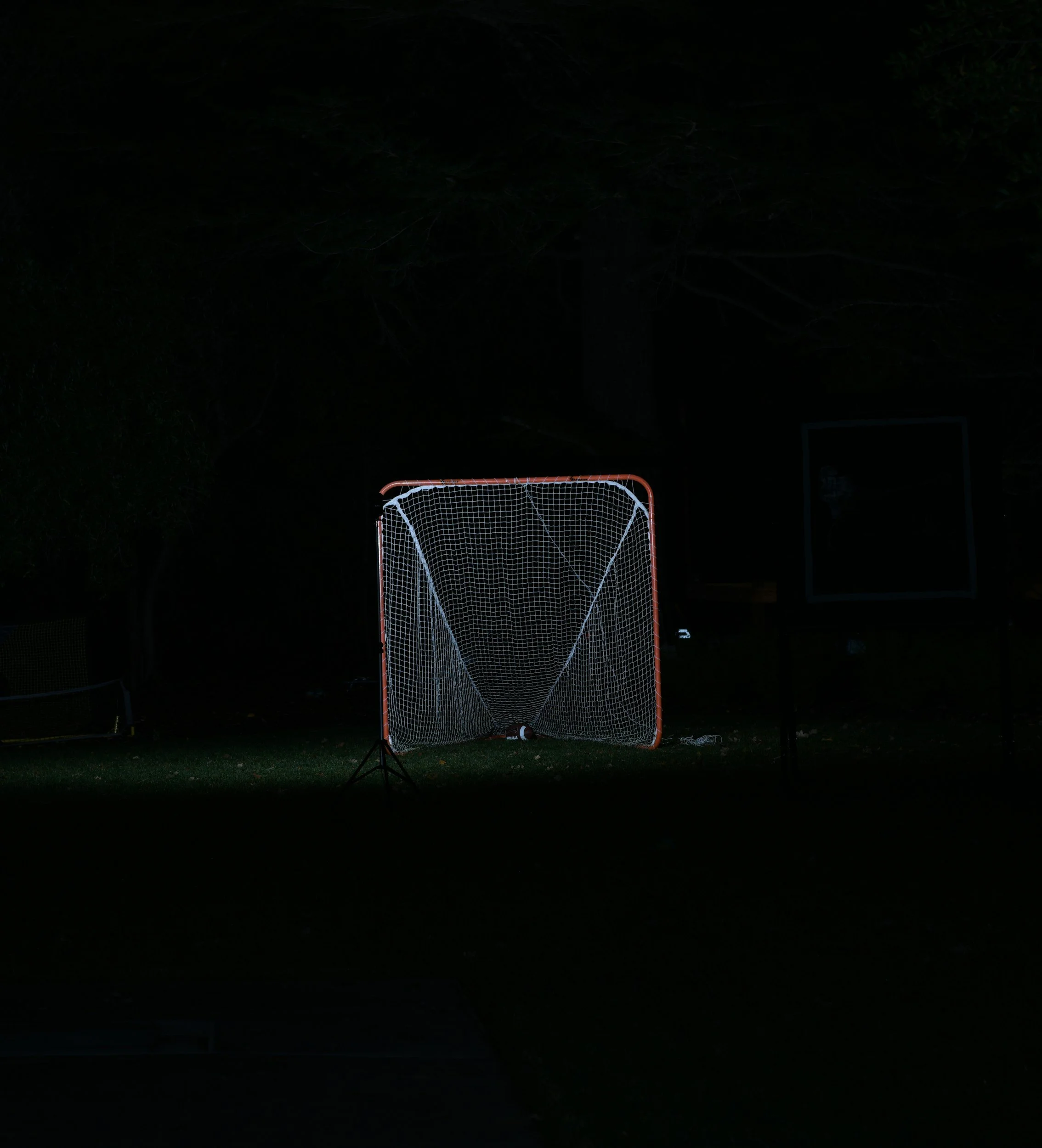 A hockey net with a hockey puck on the ground in front of it, taken at night with minimal lighting.