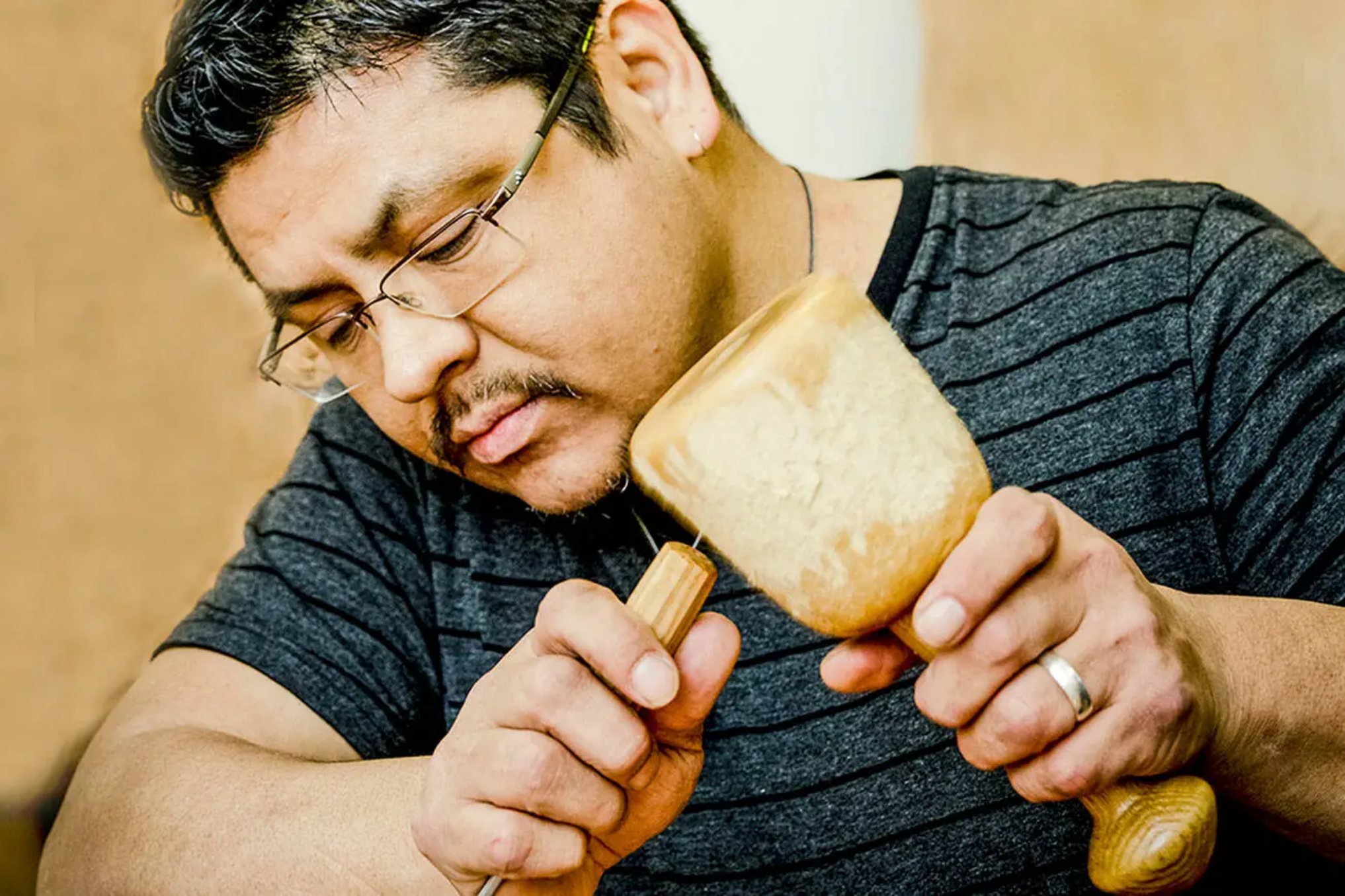 Alex McCarty northwest coast indigenous wood carver working on a totem pole with a hammer and chisel.