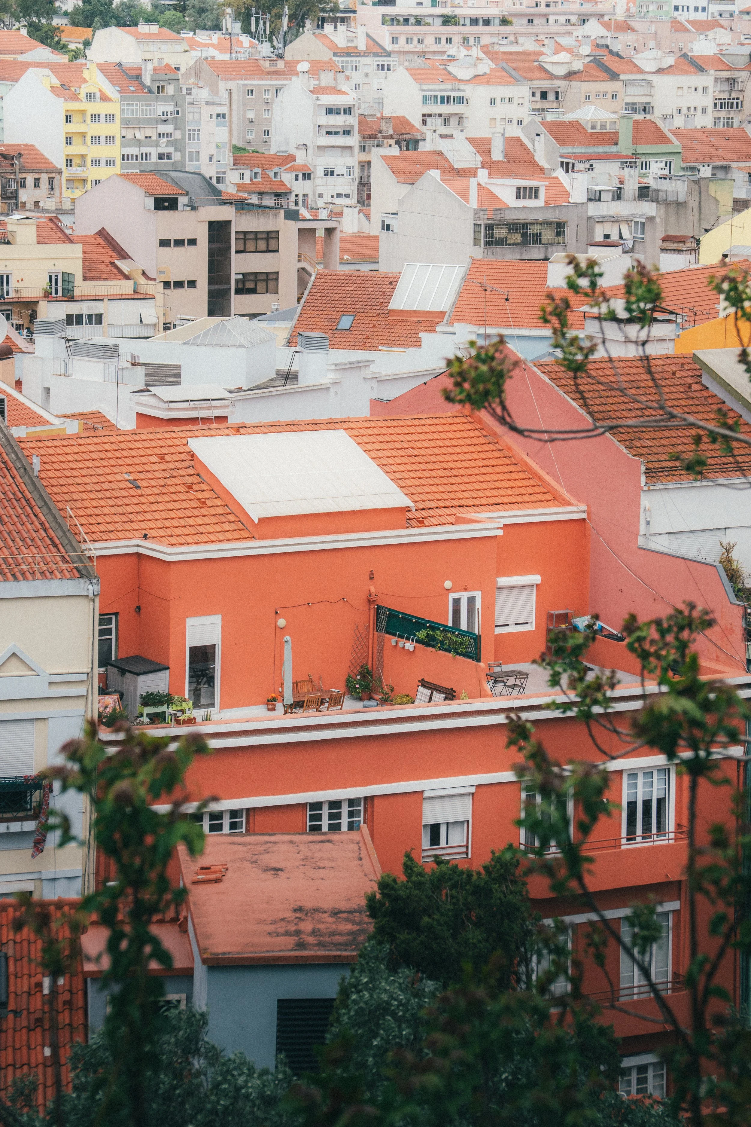 Une vue aérienne de plusieurs bâtiments résidentiels avec des toits en tuiles rouges, certains en béton et en acier, dans une zone urbaine dense.