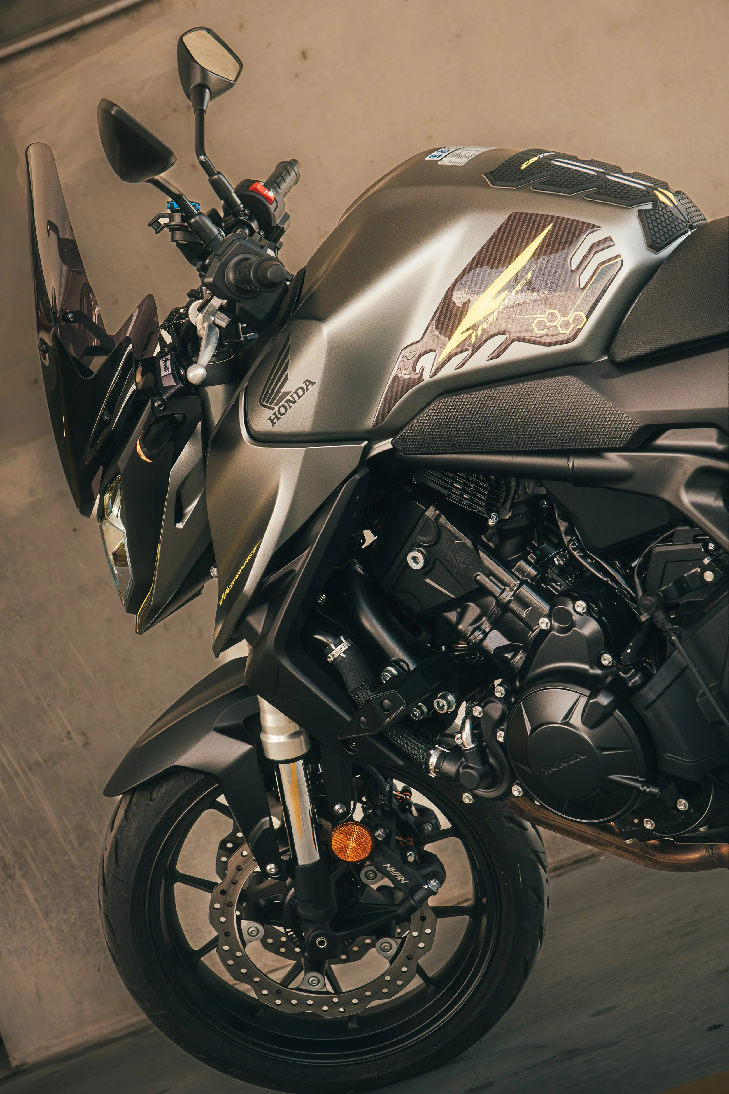 Une moto noire et grise stationnée contre un mur, avec des parties en métal, un tableau de bord, un pare-brise, et un moteur visible.
