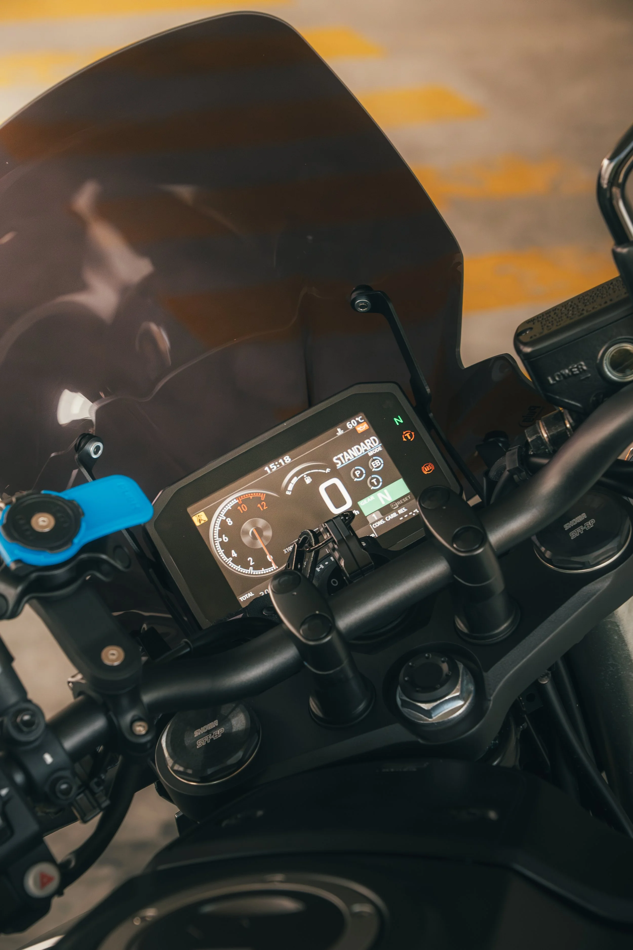 Vue du tableau de bord d'une moto, avec un écran numérique montrant des informations de vitesse, mode de conduite, et température, ainsi que le guidon et le pare-brise.