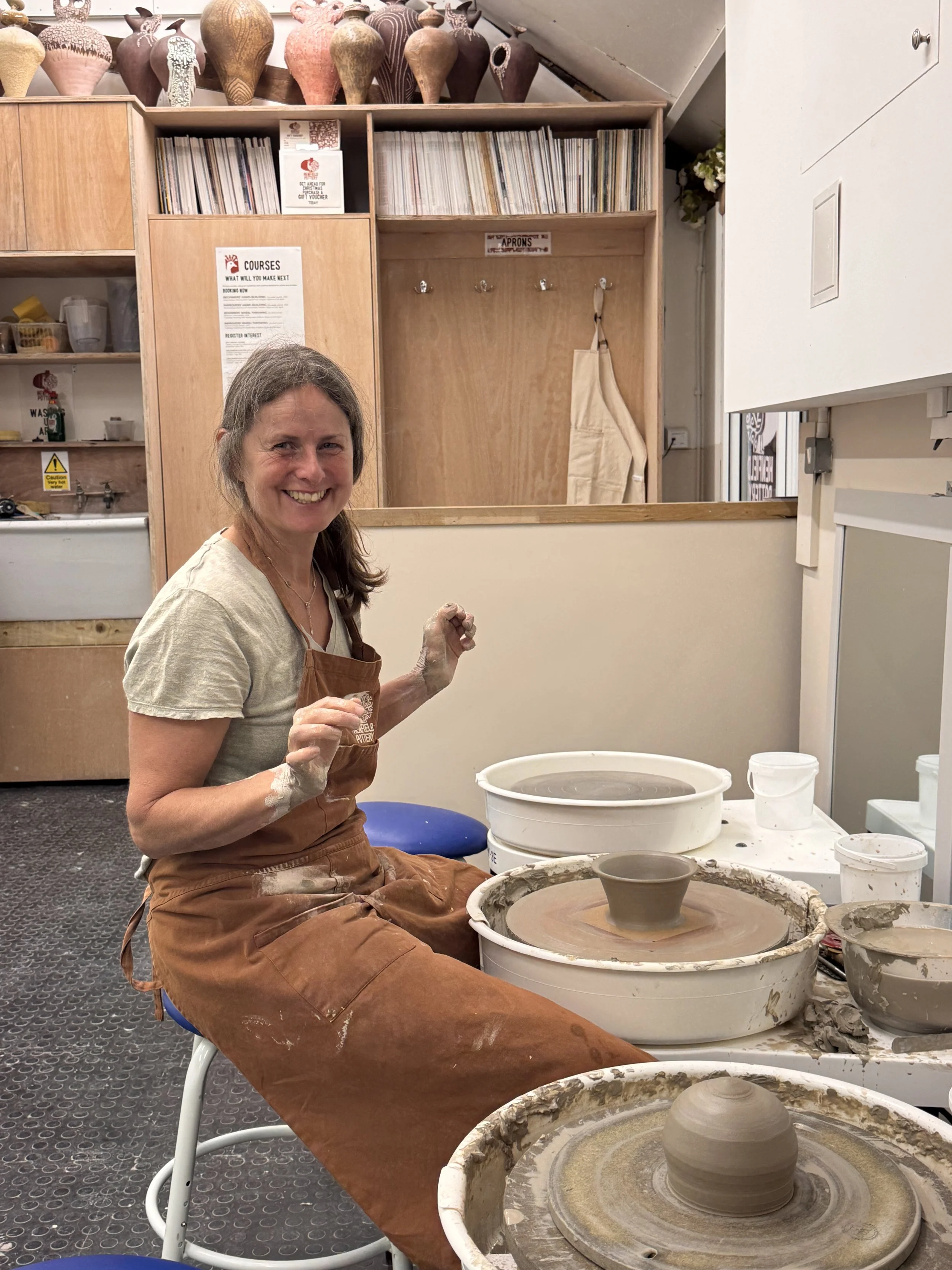Henfield Pottery student sitting at a pottery wheel in the Henfield Pottery Studio with a piece she's thrown