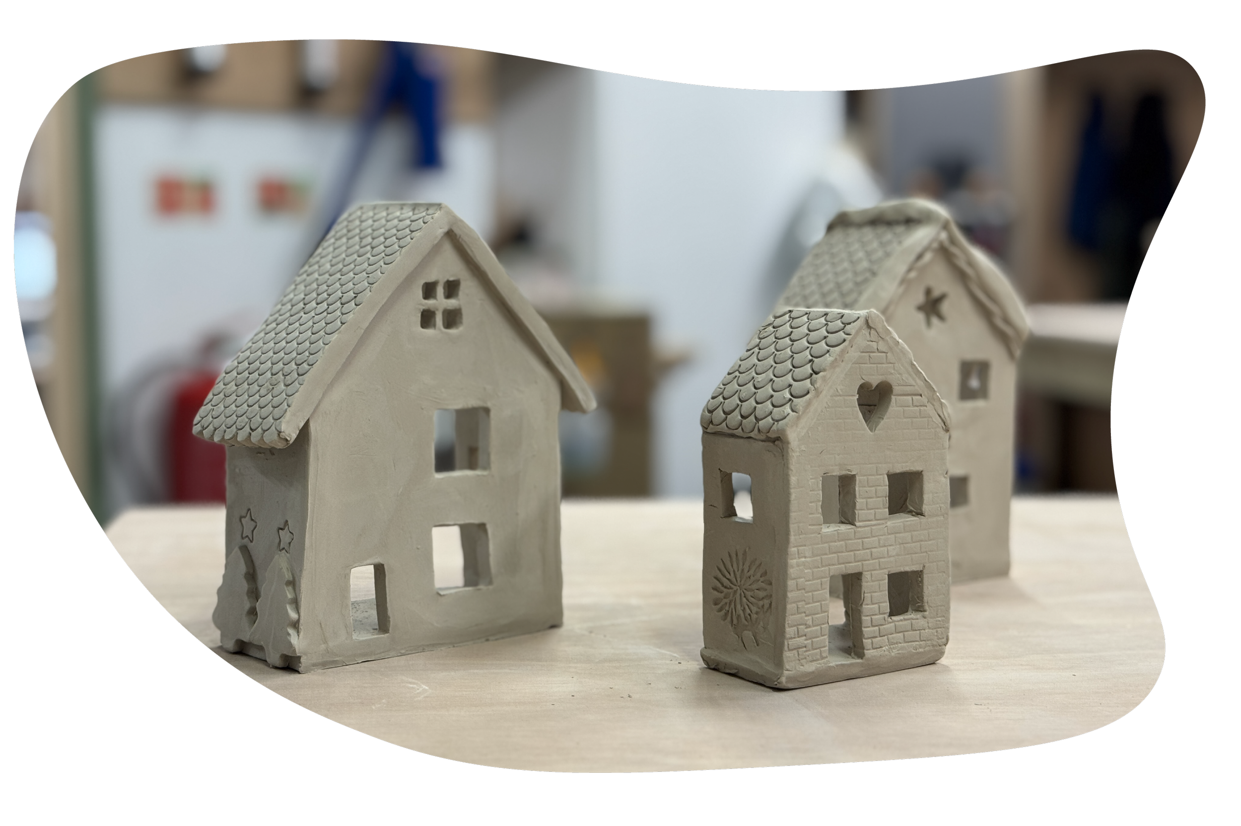 Several small ceramic tea-light house with different window shapes and roof designs, placed on a wooden surface made by Henfield Pottery students