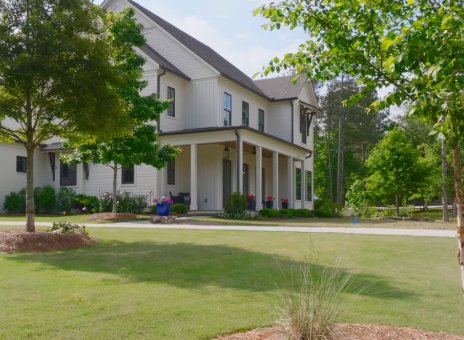 A large white house with a wrap-around porch surrounded by green trees and a well-maintained lawn.