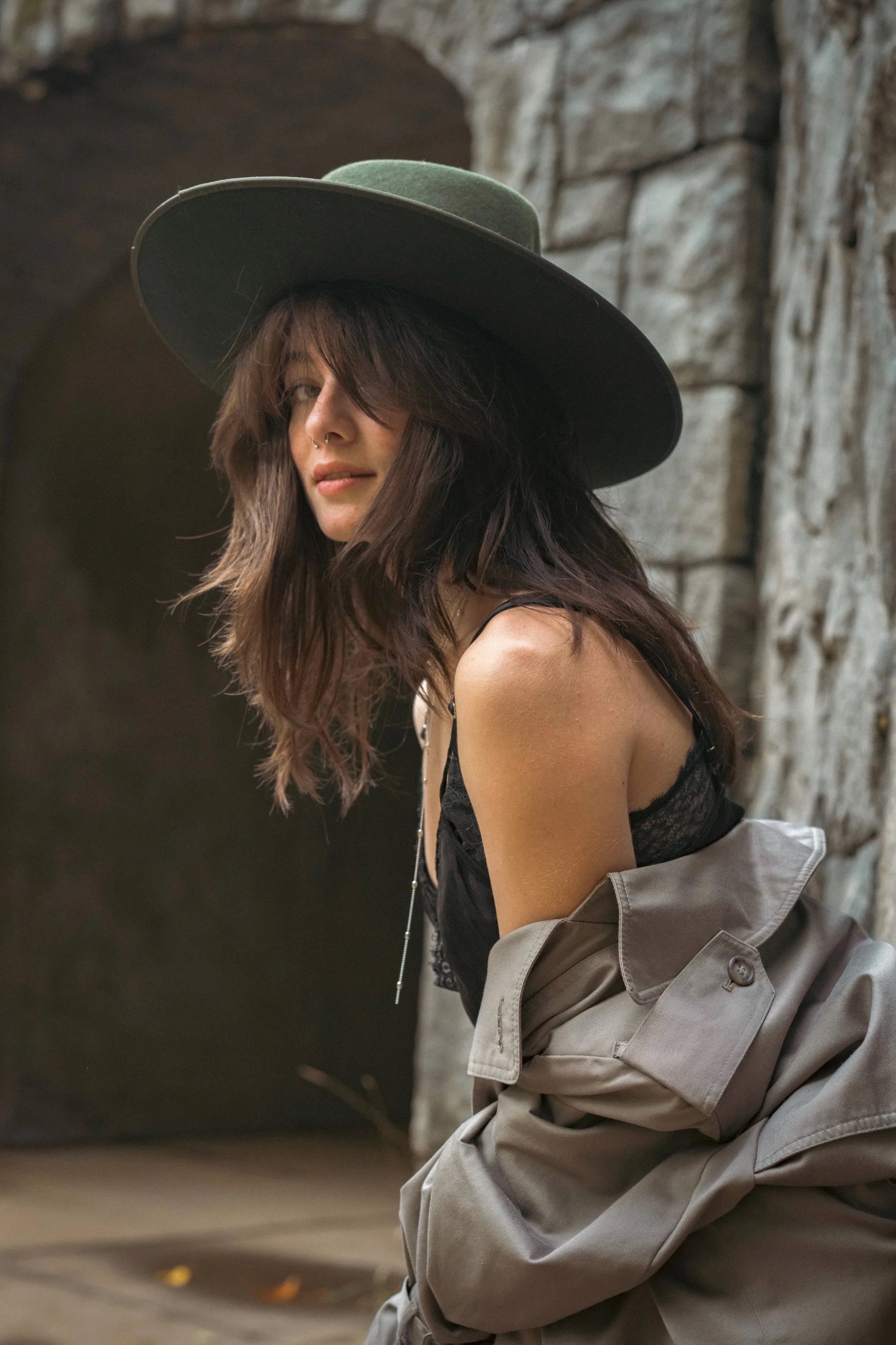 Woman in green wide brim hat leaning against ancient stone wall in dappled sunlight, intimate editorial portrait photography by Missoula Montana photographer