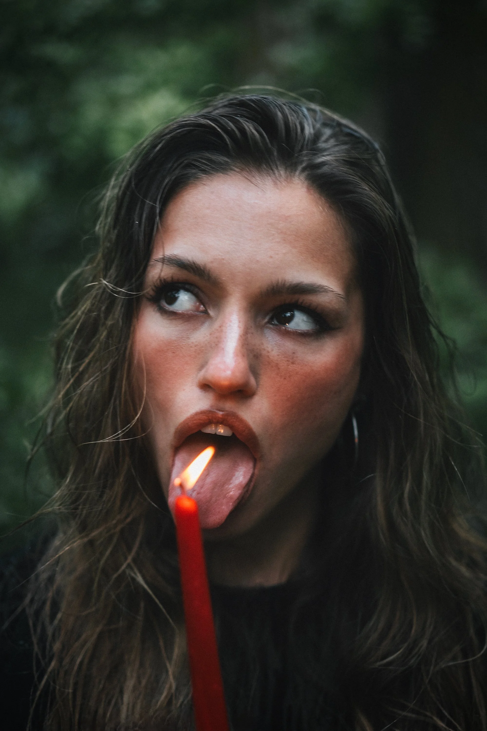 Close up portrait of woman licking a lit candle flame in a dark forest, bold creative portrait photography by Missoula Montana photographer