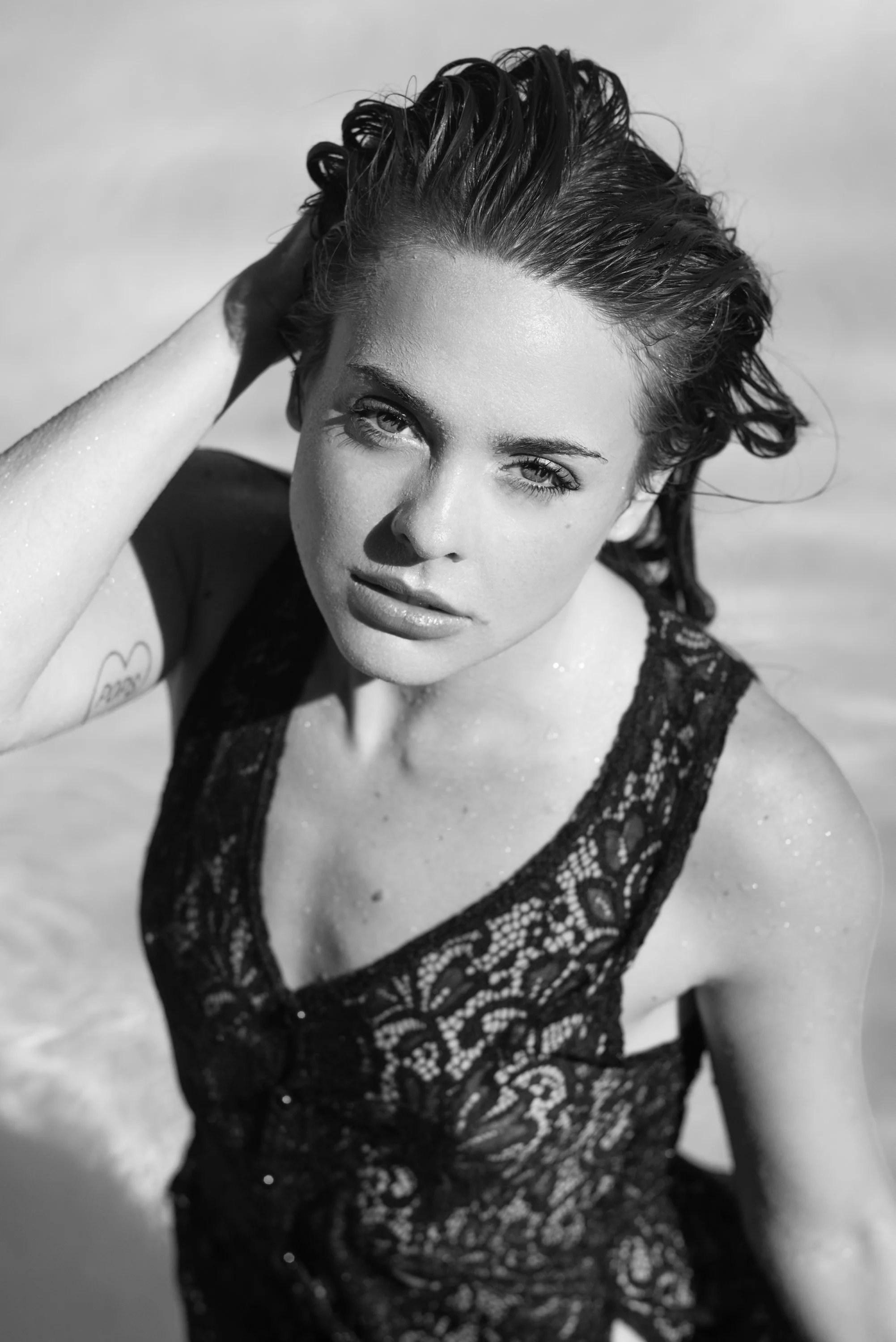 A woman with wet hair and water drops on her skin, wearing a lace swimsuit, posing outdoors.