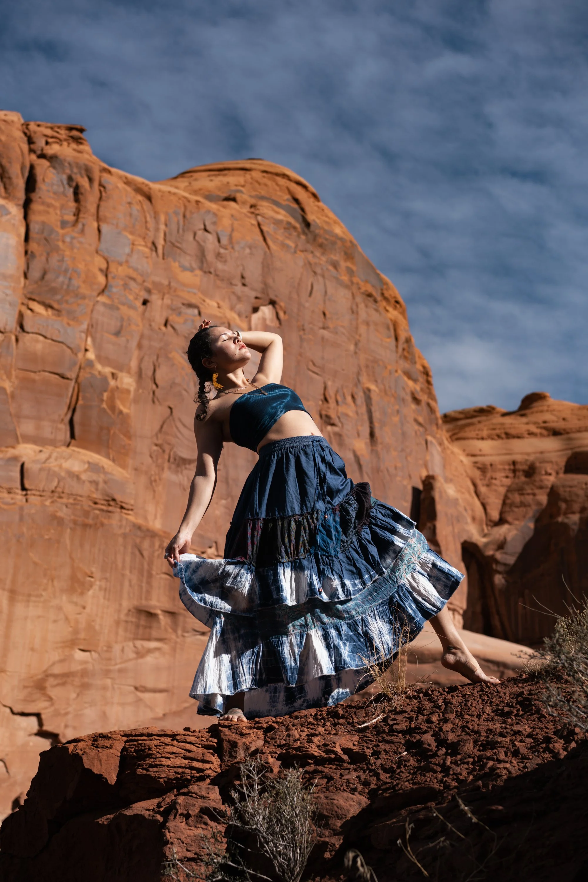 Woman dancing in a flowing blue skirt among red rock formations in the desert, outdoor portrait photography by Montana photographer.