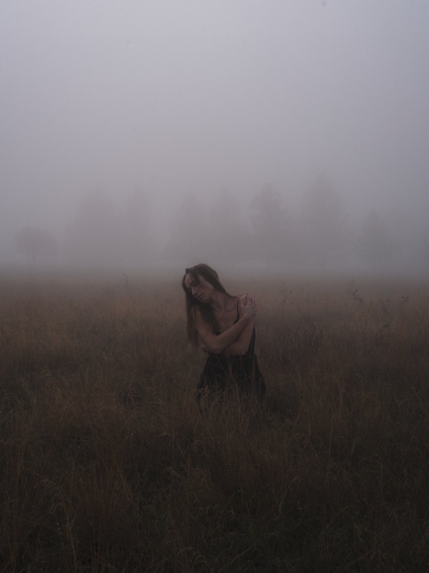Self portrait of woman standing alone in a foggy dry grass field with arms crossed in moody atmospheric light, artistic photography by Missoula Montana photographer