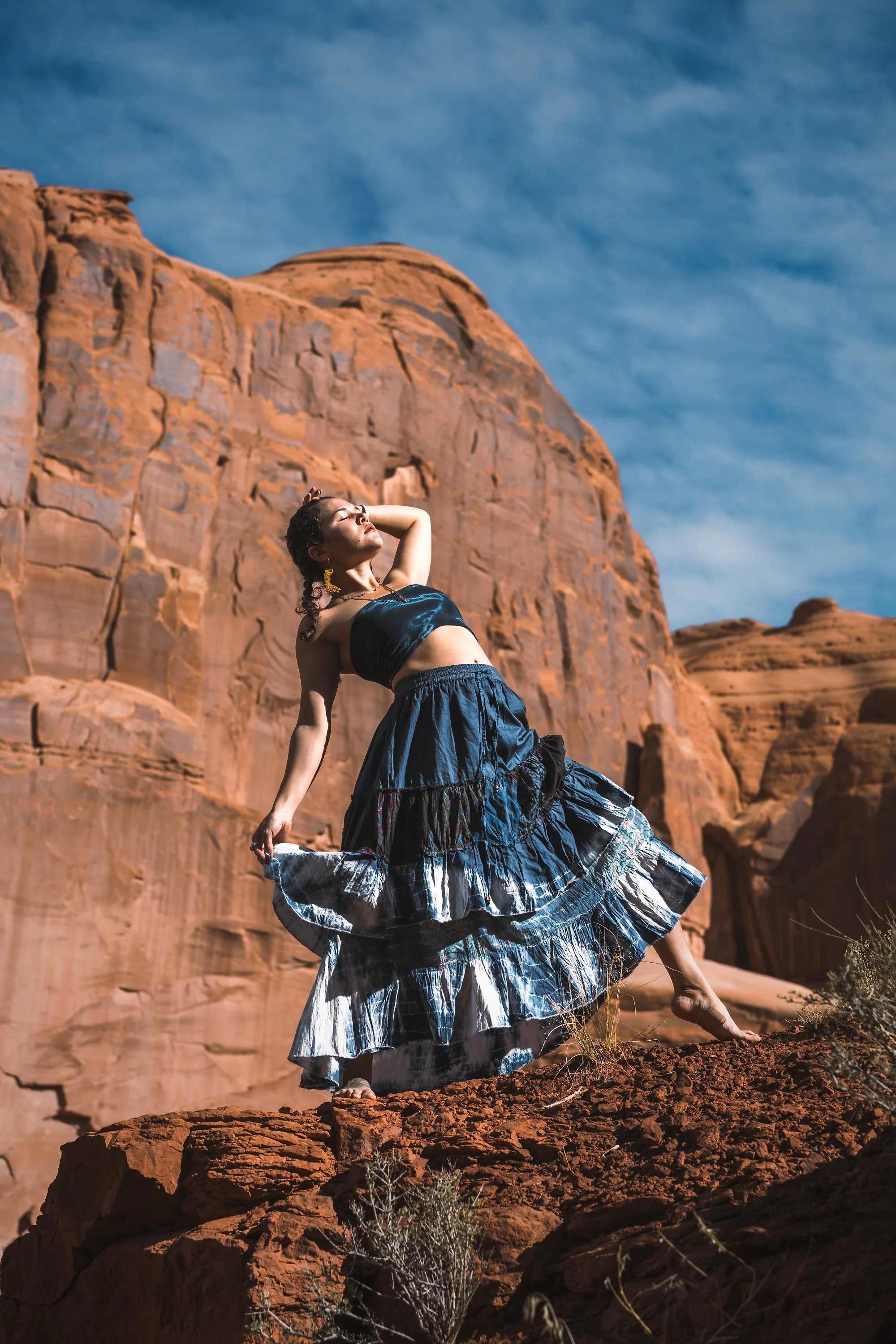 Woman dancing in a flowing blue skirt among red rock formations in the desert, outdoor portrait photography by Montana photographer