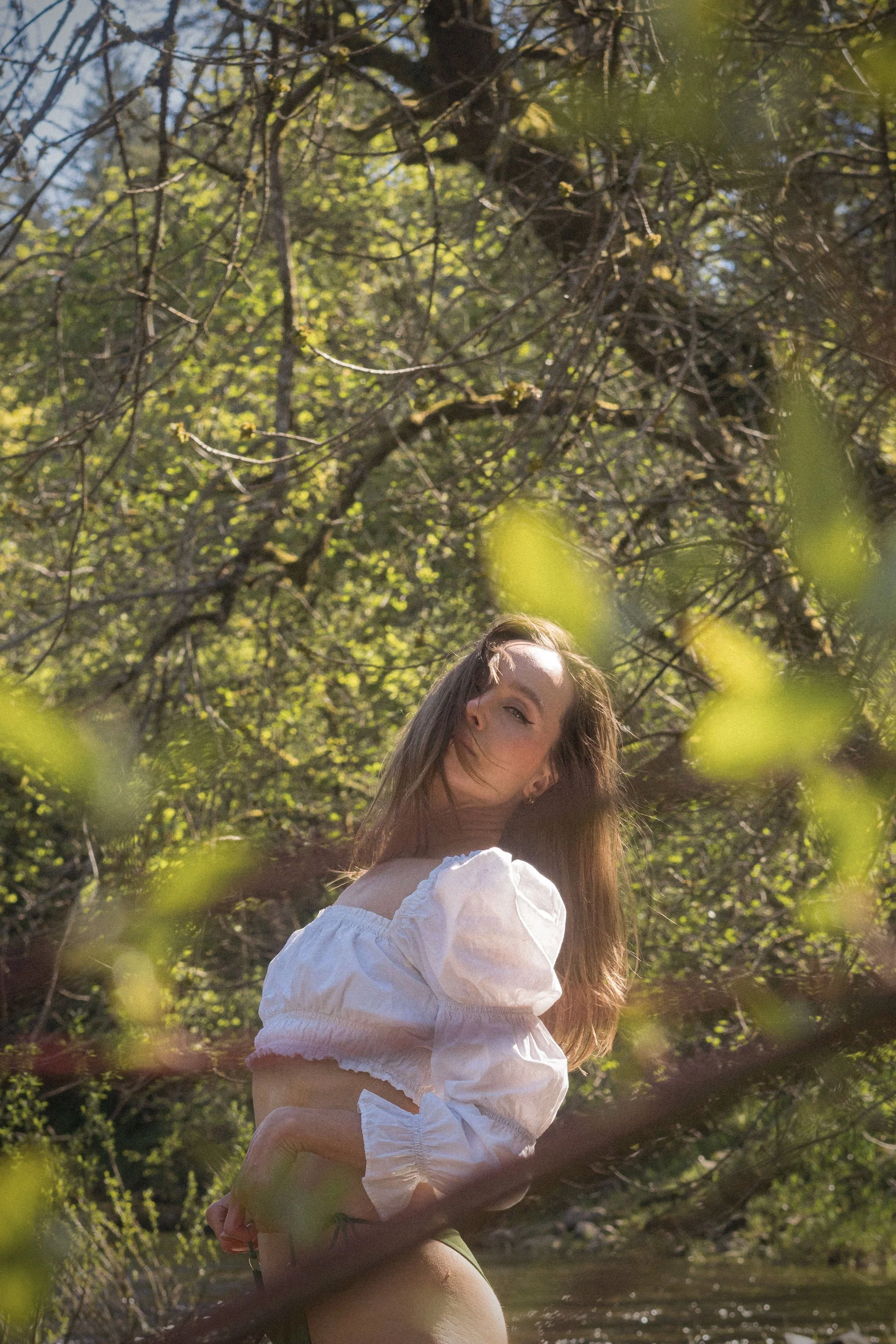 Woman in white puff sleeve top photographed through spring tree branches in golden light, self portrait by Missoula Montana photographer