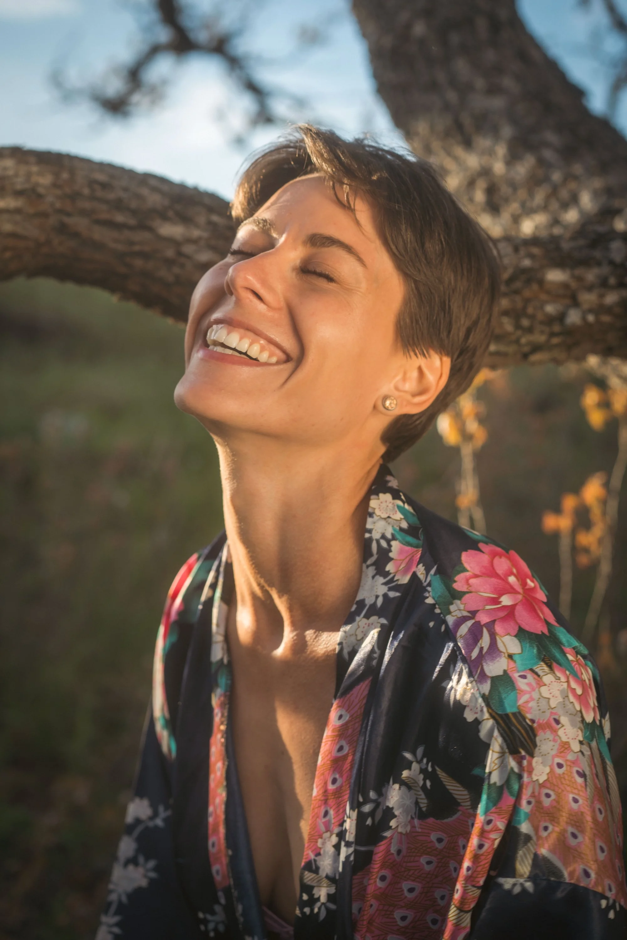 Woman laughing in golden light outdoors leaning against a tree, portrait photography Missoula Montana