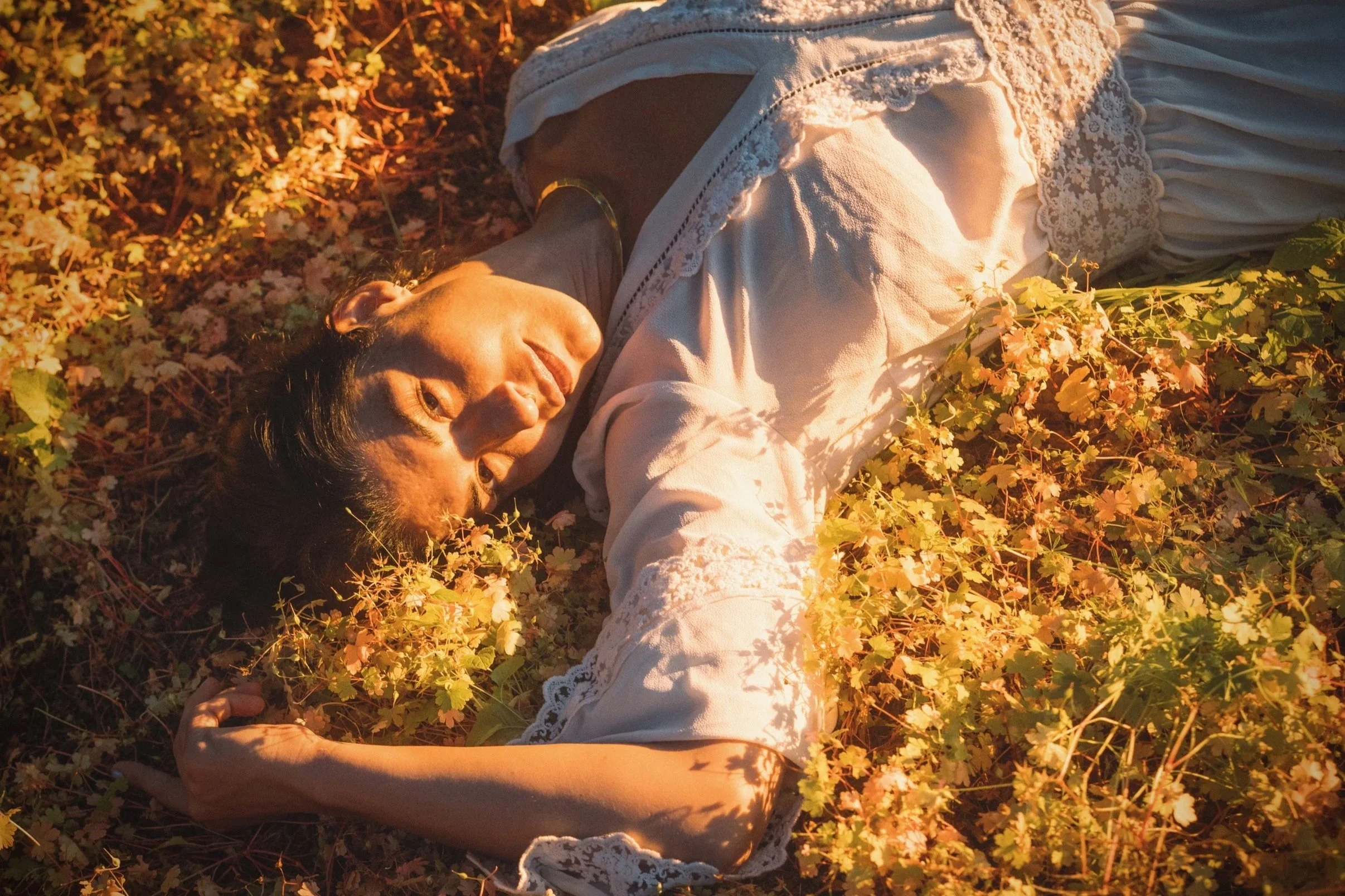 Woman in white lace dress lying in golden autumn leaves in warm evening light, intimate portrait photography by Missoula Montana photographer