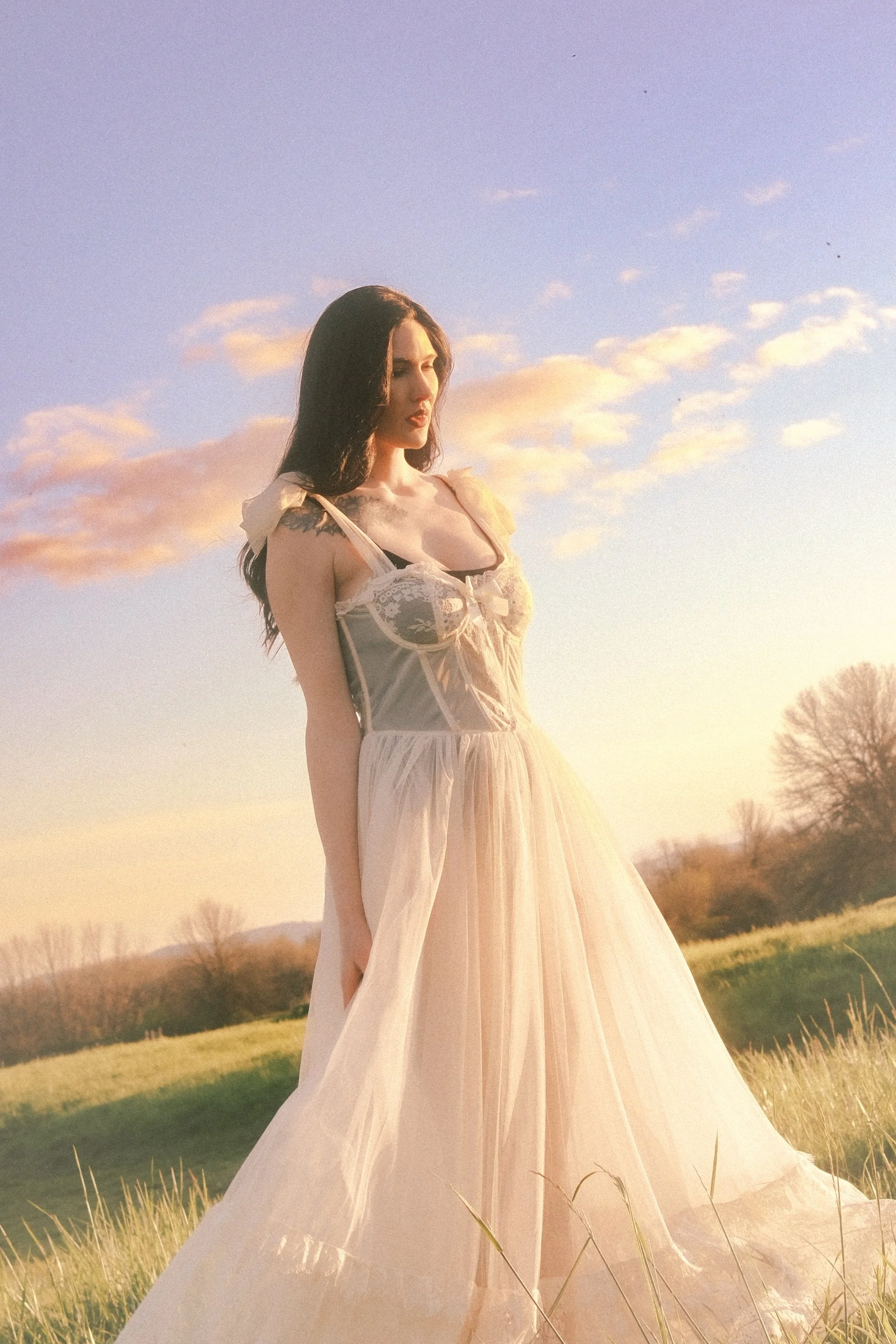 Woman in flowing sheer dress standing in a field at golden hour with a glowing sunset sky, ethereal portrait photography by Missoula Montana photographer