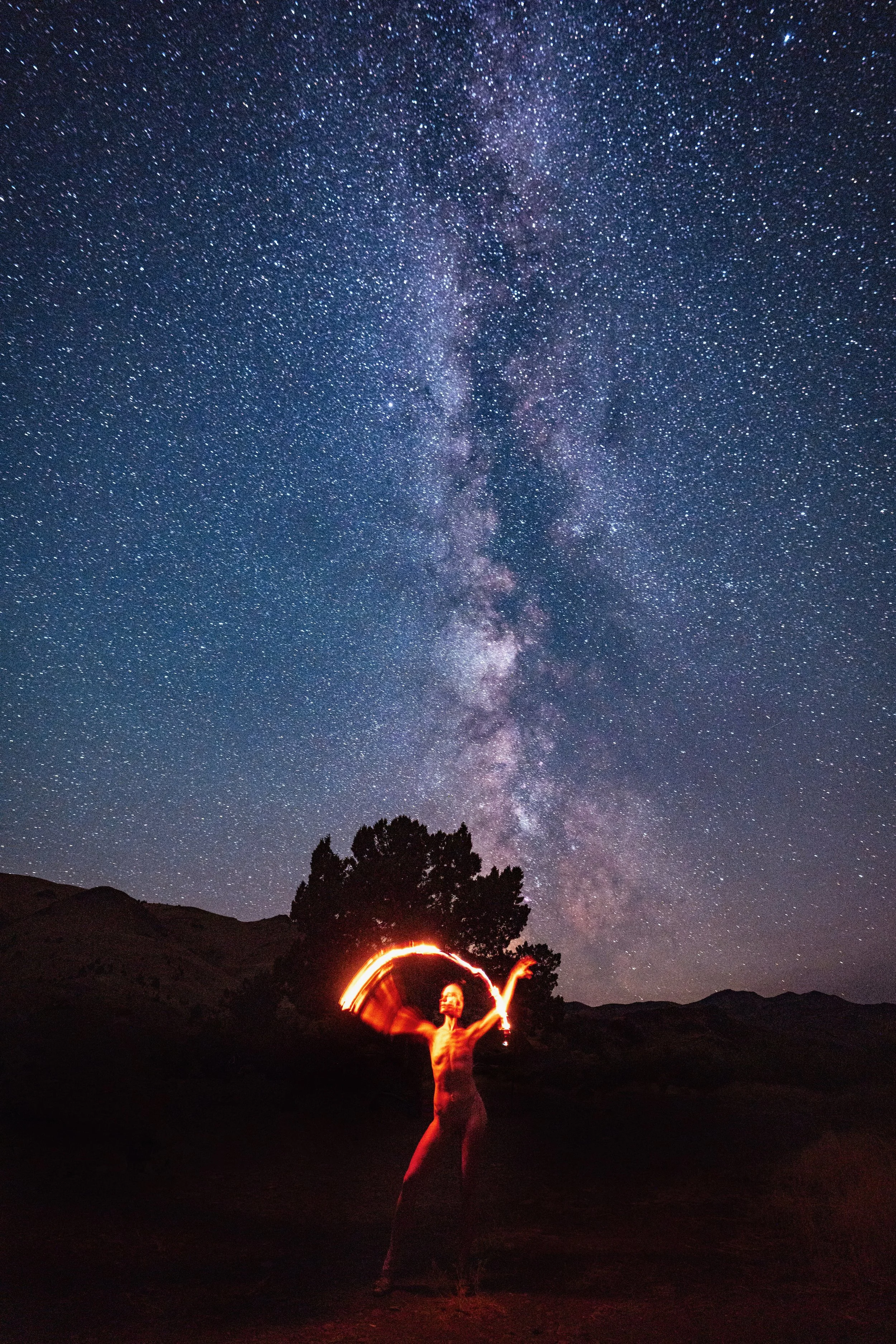 Self portrait of woman spinning fire under the Milky Way galaxy on a dark Montana night, long exposure fine art photography by Missoula Montana photographer