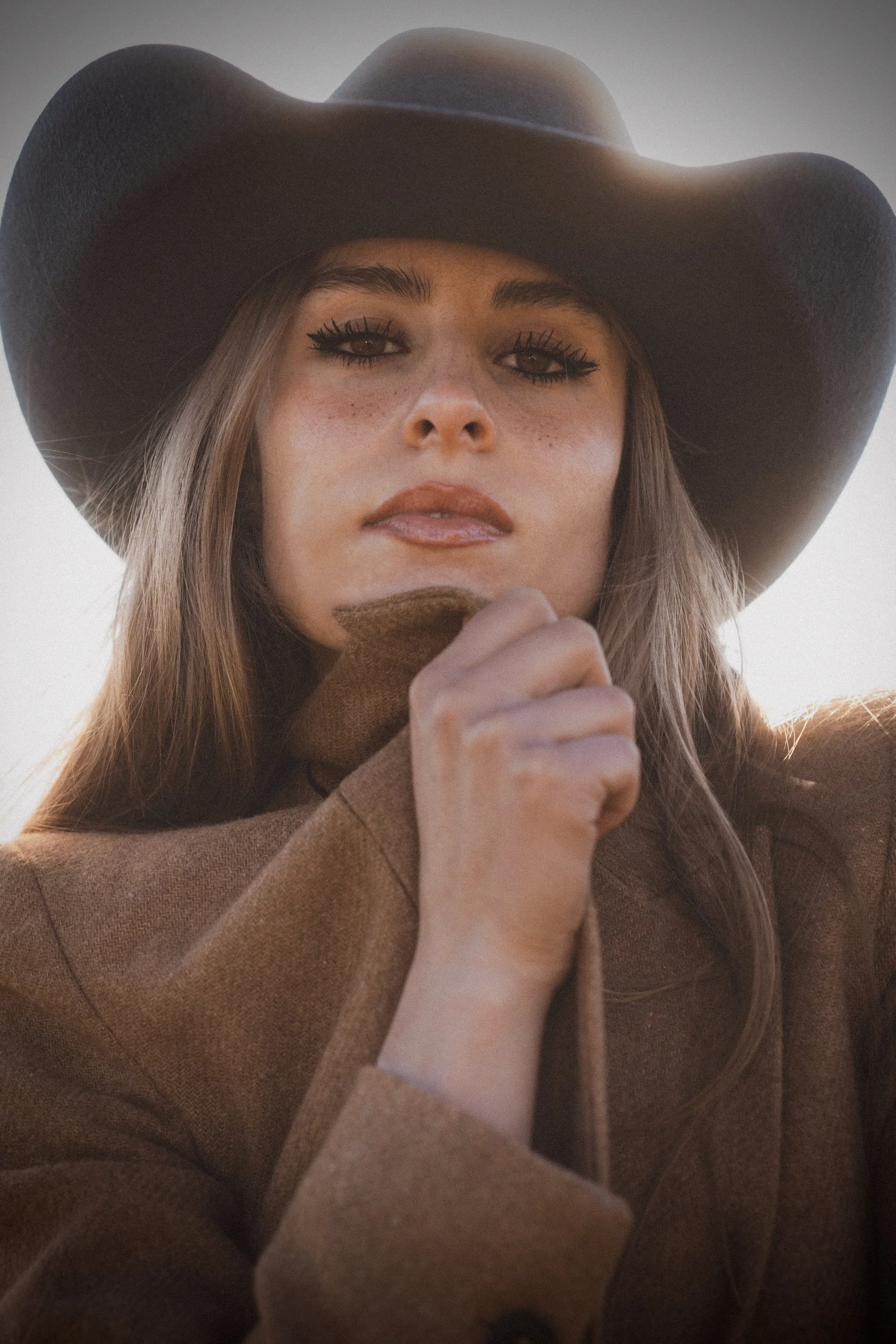 Close up portrait of woman in black cowboy hat with freckles and direct gaze in warm backlit light, fine art portrait photography by Missoula Montana photographer
