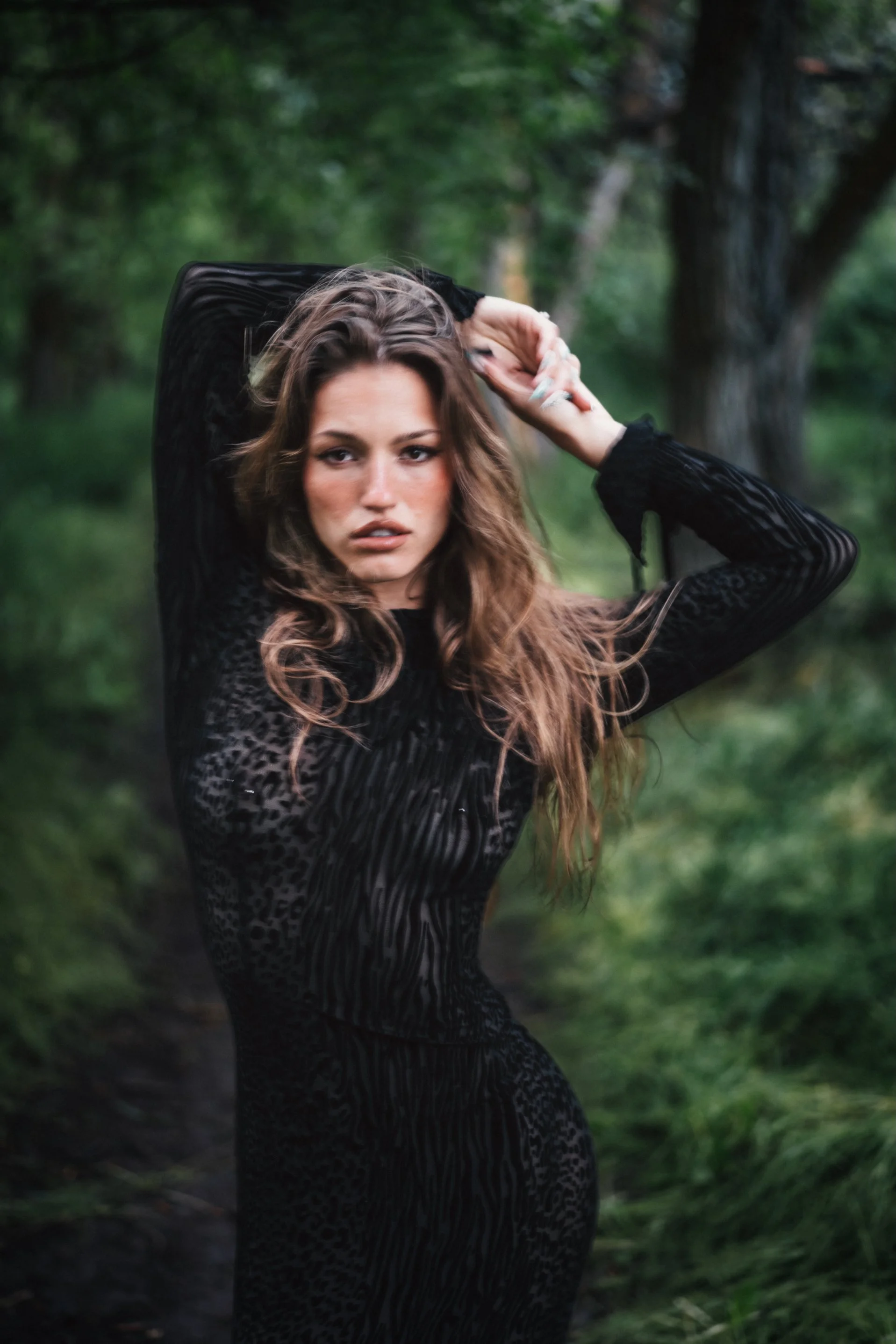 Woman in black dress with direct gaze standing on a lush green forest path with windswept hair, bold fine art portrait photography by Missoula Montana photographer