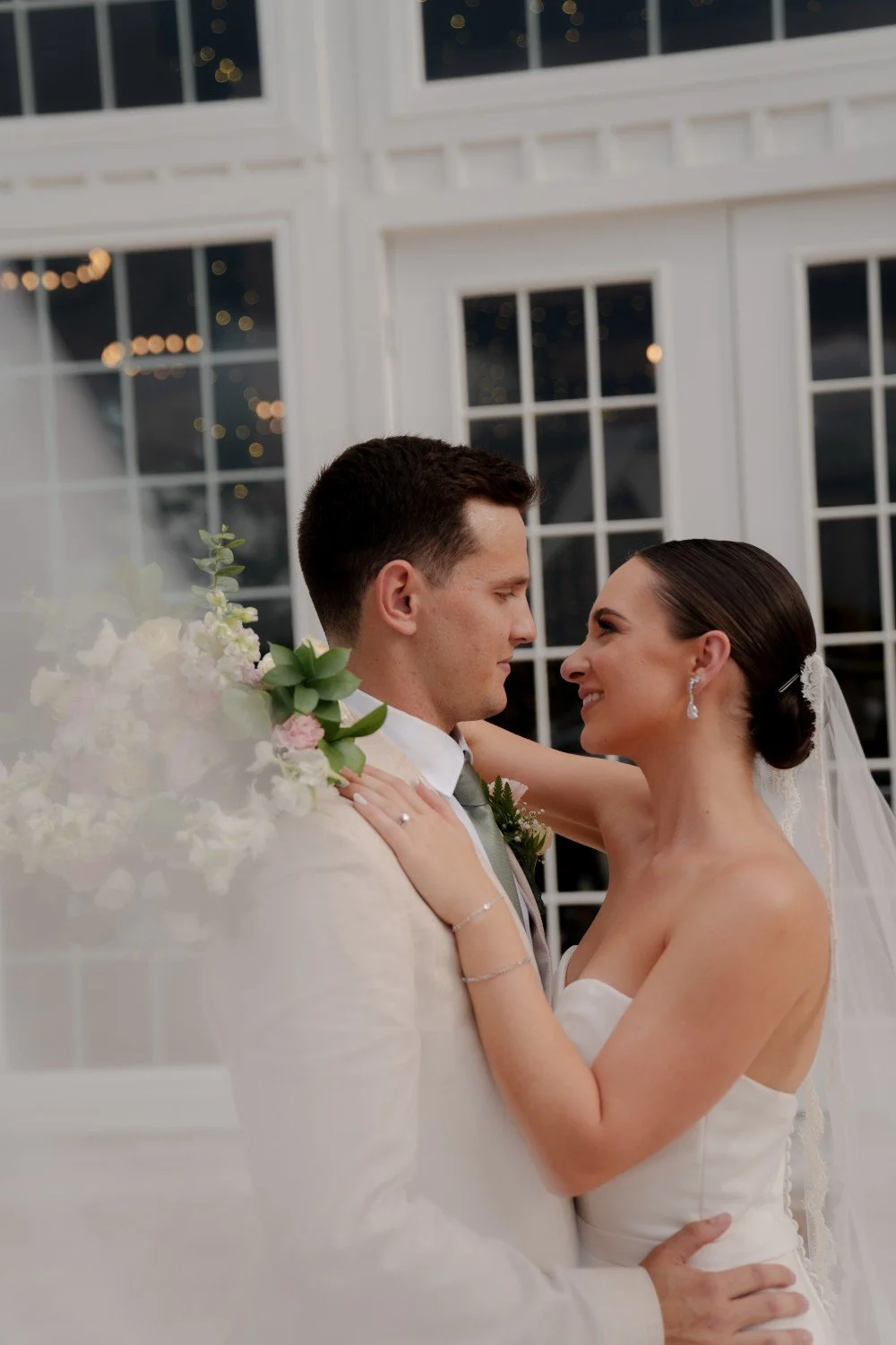 A bride and groom dance closely during their wedding reception in a well-lit indoor venue with large windows.