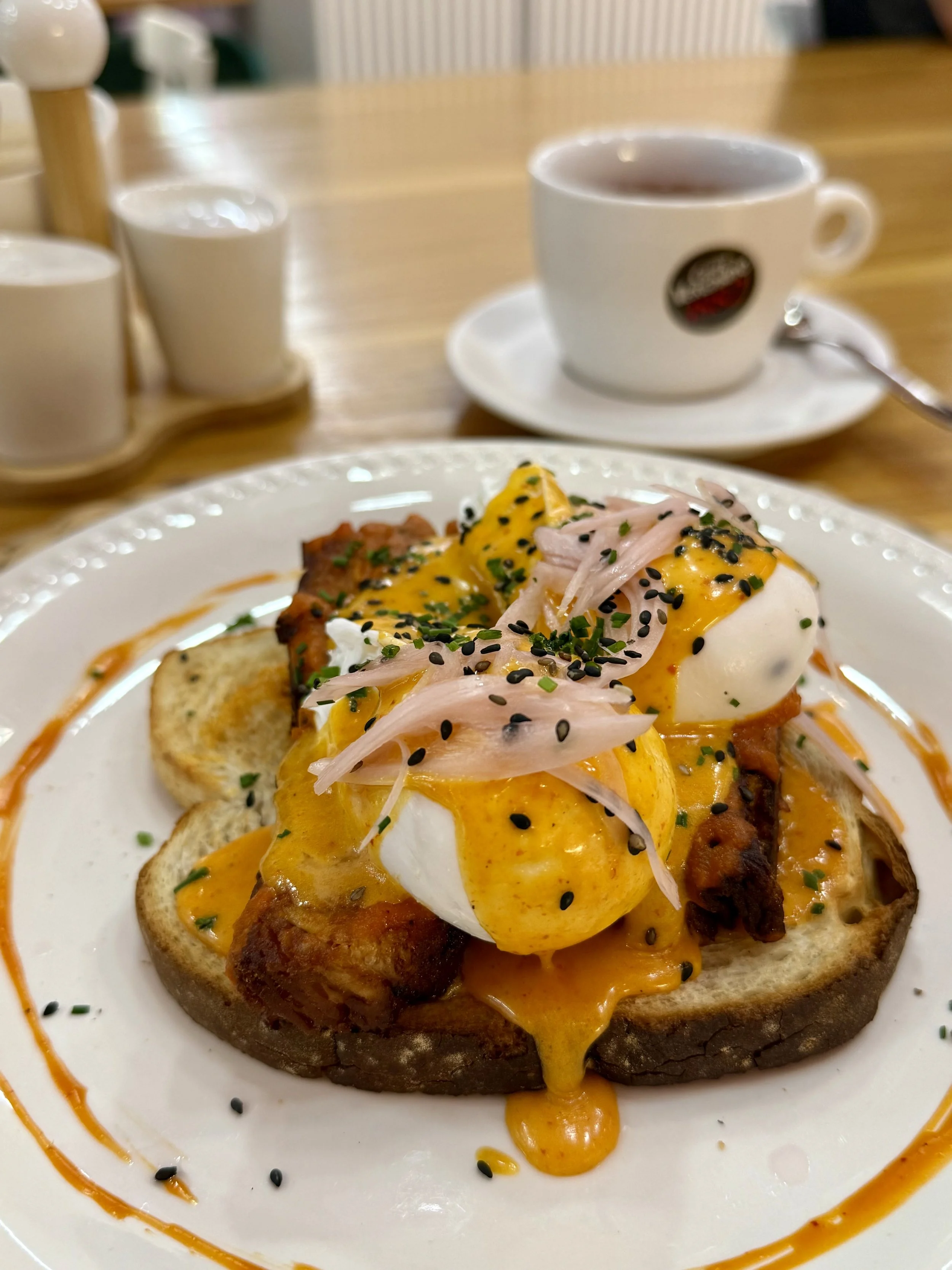 Poached eggs with hollandaise sauce, black sesame seeds, chives, served on toasted bread with a side of a baked breakfast potato.