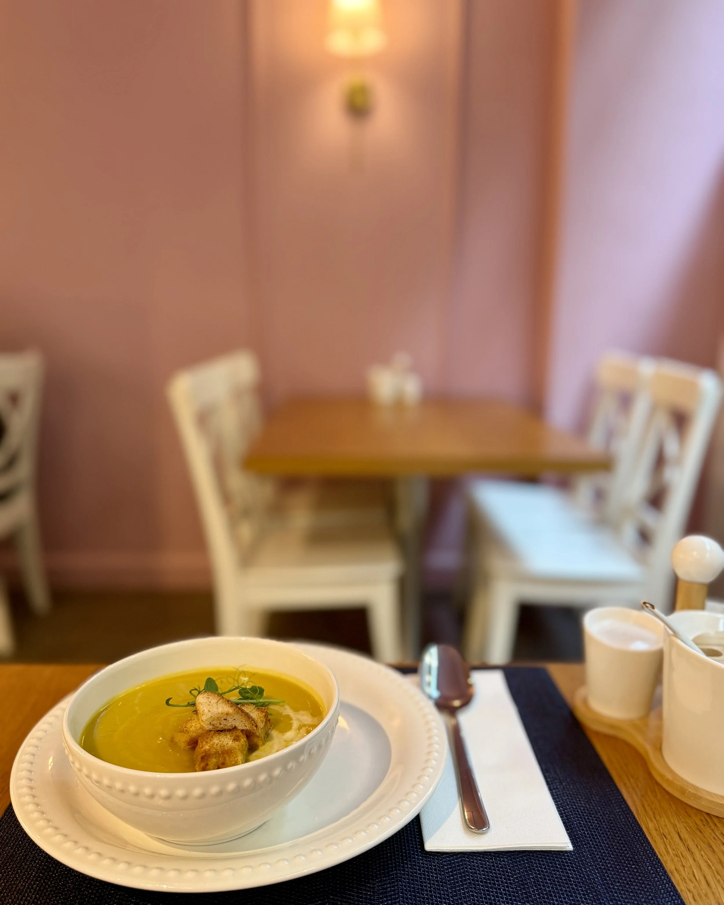 A bowl of soup with croutons and herbs on a plate, set on a table with cutlery and a cup of water nearby.