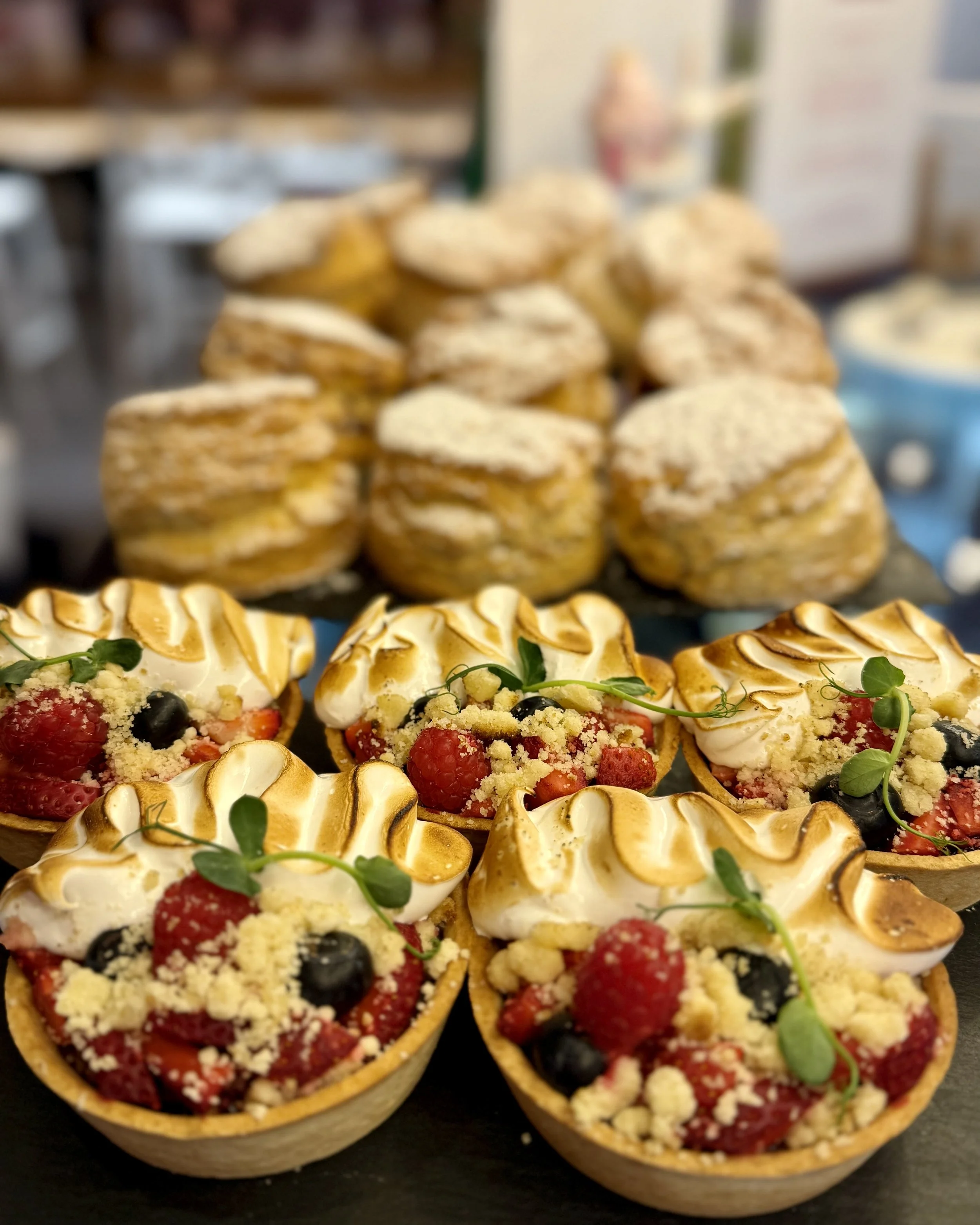 Dessert cups filled with fresh berries, crumb topping, and garnished with microgreens, arranged on a black surface.