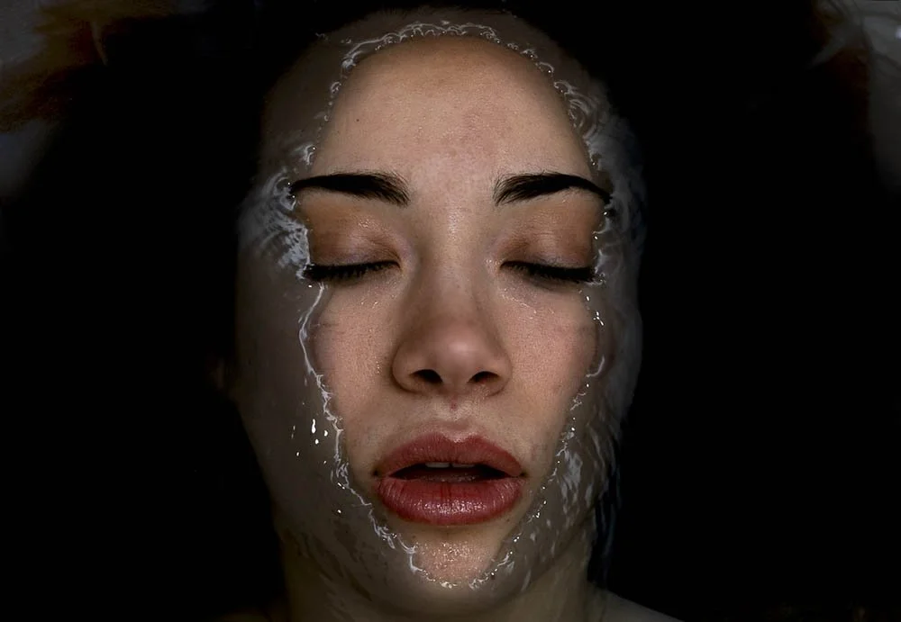 Close-up of a woman's face with eyes closed, partially submerged in water.