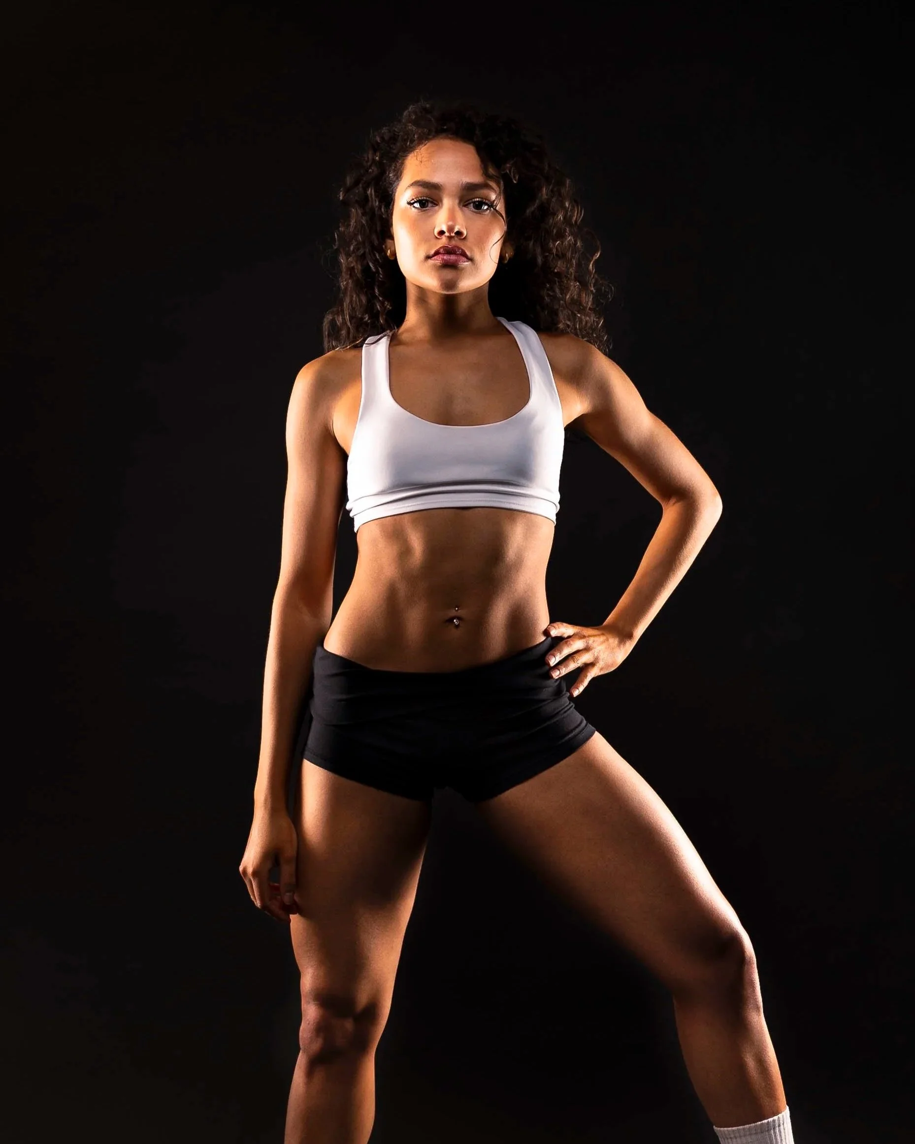 Dance image with dark and contrasted lighting to accentuate figure and muscles. Model is in an Alo sports bra.