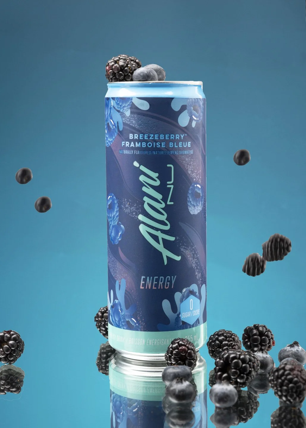 A tall can of Alien Energy drink with blackberry flavor, surrounded by fresh blackberries and blueberries, on a reflective surface with a blue background.