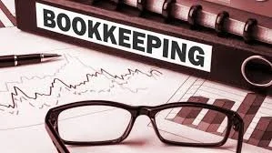 A desk with a sign labeled 'Bookkeeping', a financial chart, a pair of glasses, a pen, and a calculator.