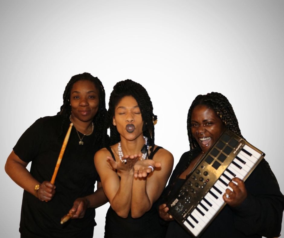 Three women posing with musical instruments and making playful expressions against a plain background.