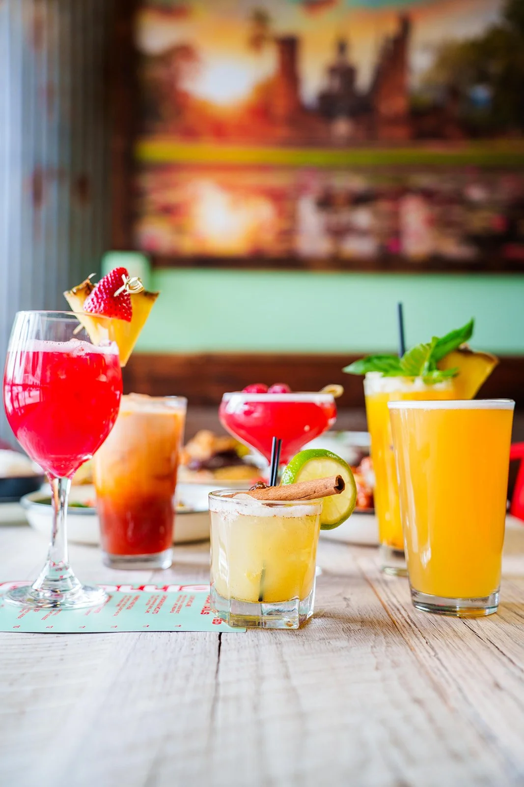 A variety of colorful cocktails on a wooden table in a bright setting.