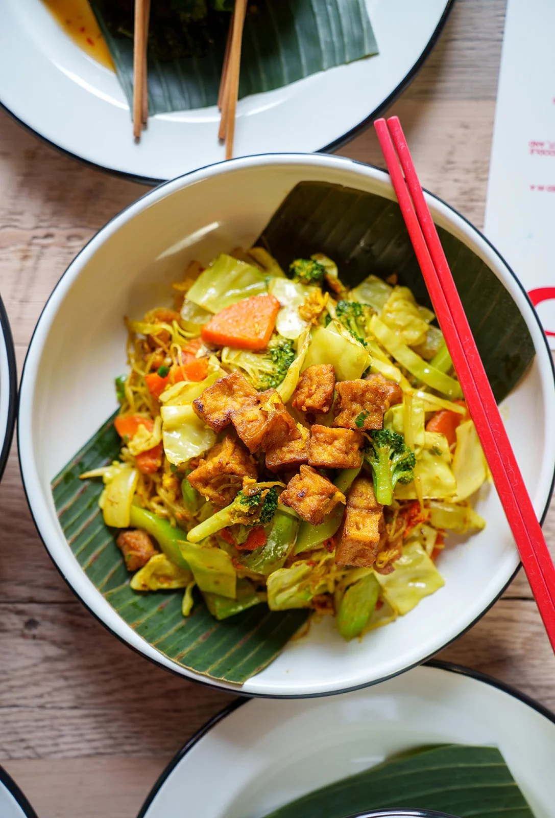 Bowl of stir-fried vegetables with tofu on a banana leaf, with chopsticks resting on the rim.