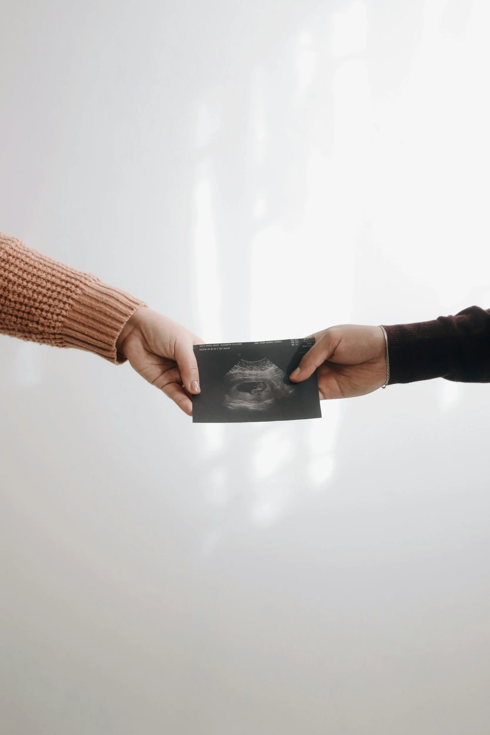 Two hands each holding an ultrasound picture, presents against a plain white background.