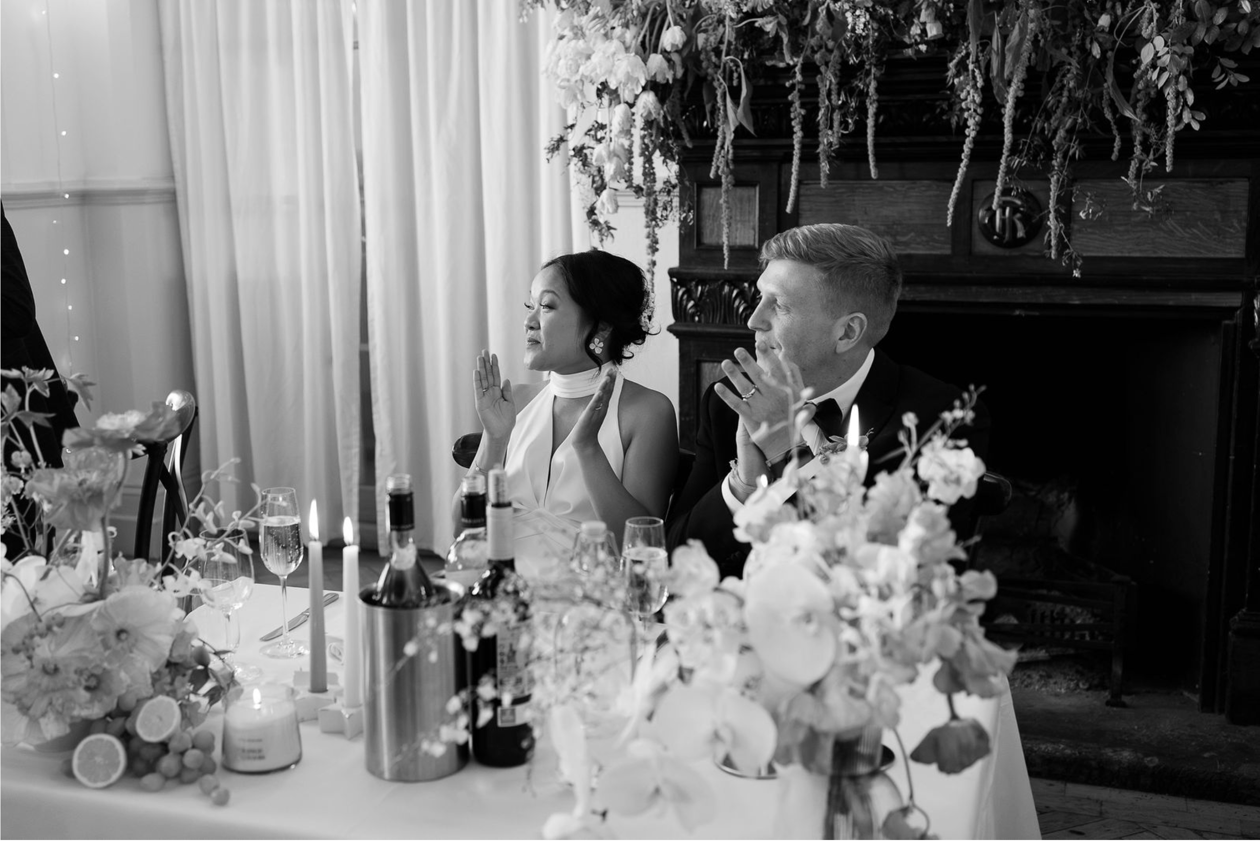A couple at a wedding reception, blowing out candles on a cake, surrounded by floral decorations.