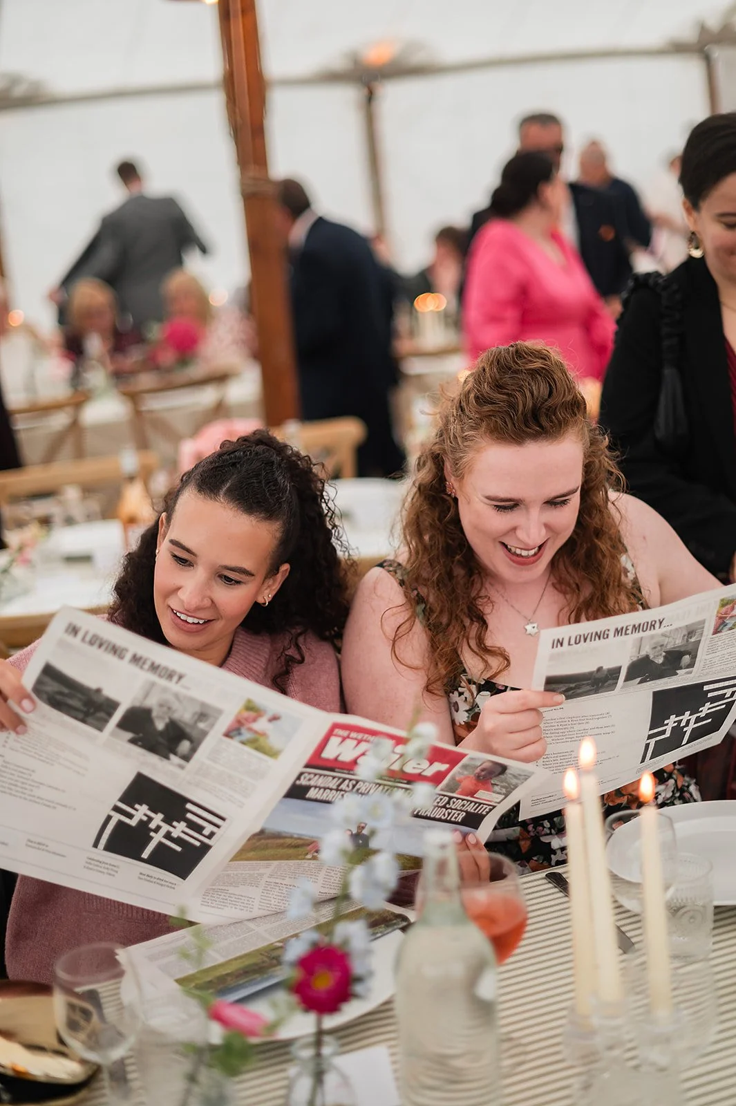 Two guests sitting at a wedding breakfast reading newspapers, smiling and enjoying themselves.