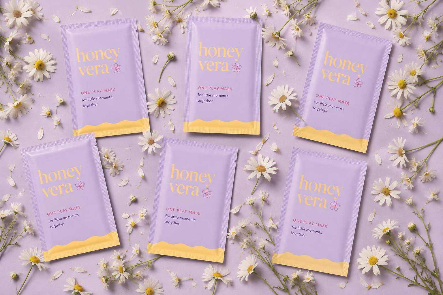 Six lavender-colored packets of honey vera One Play Mask arranged on a purple surface, surrounded by scattered white daisy flowers and petals.