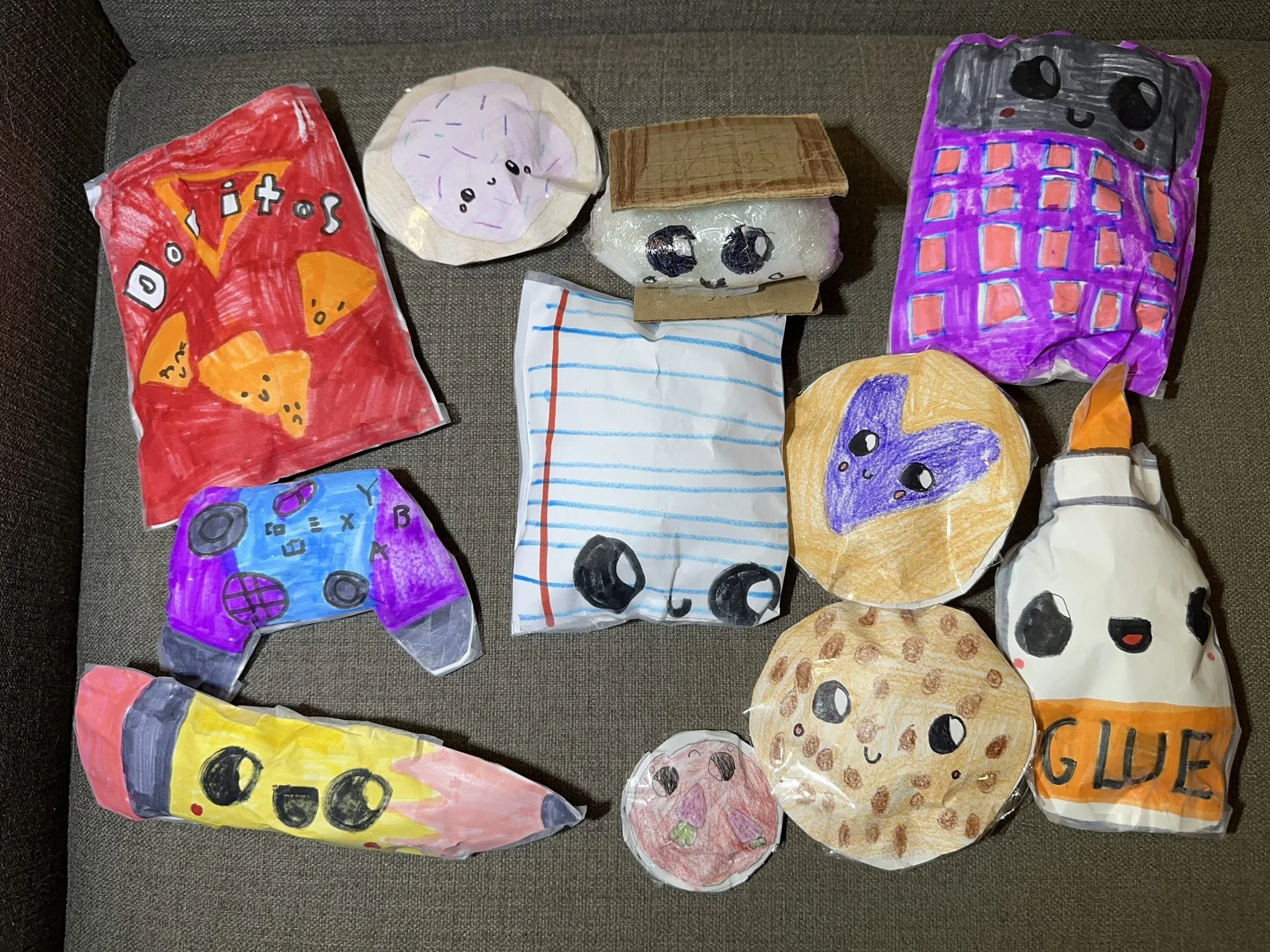 Colorful, hand-painted paper bags resembling various animals with smiley faces, arranged on a gray fabric surface.