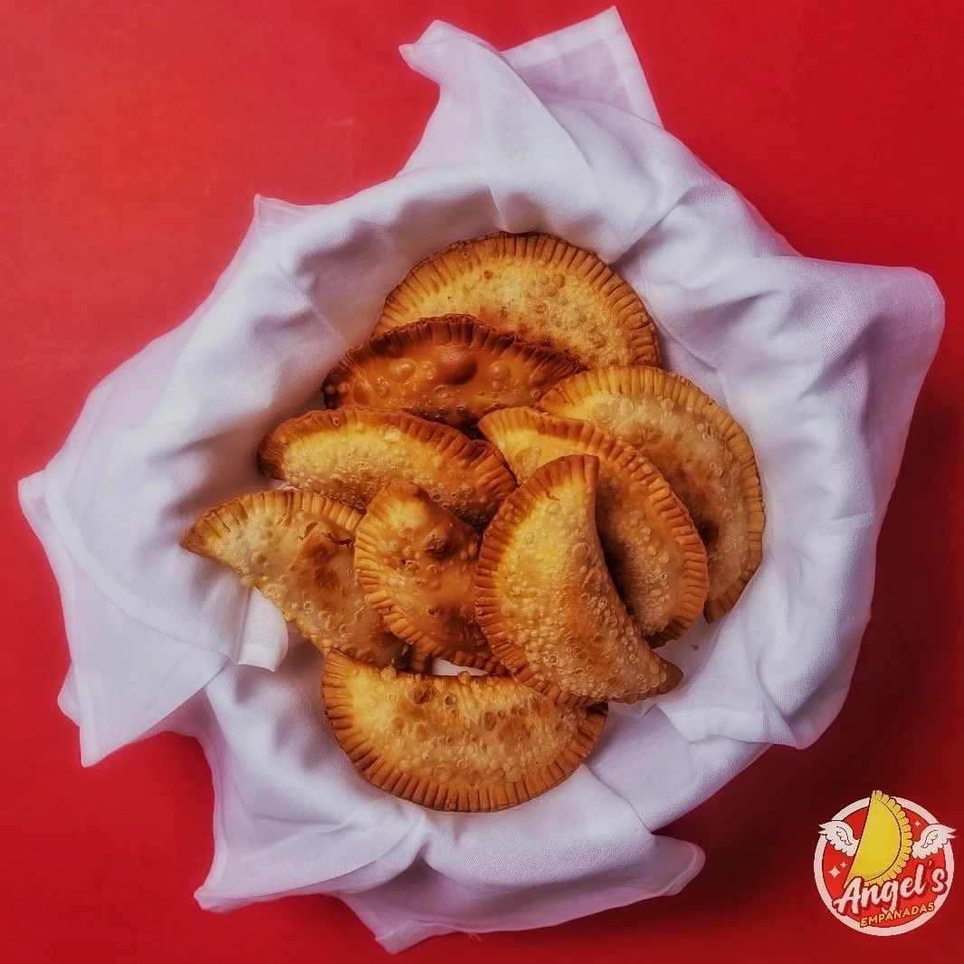 Basket of golden empanadas on white cloth against a red background