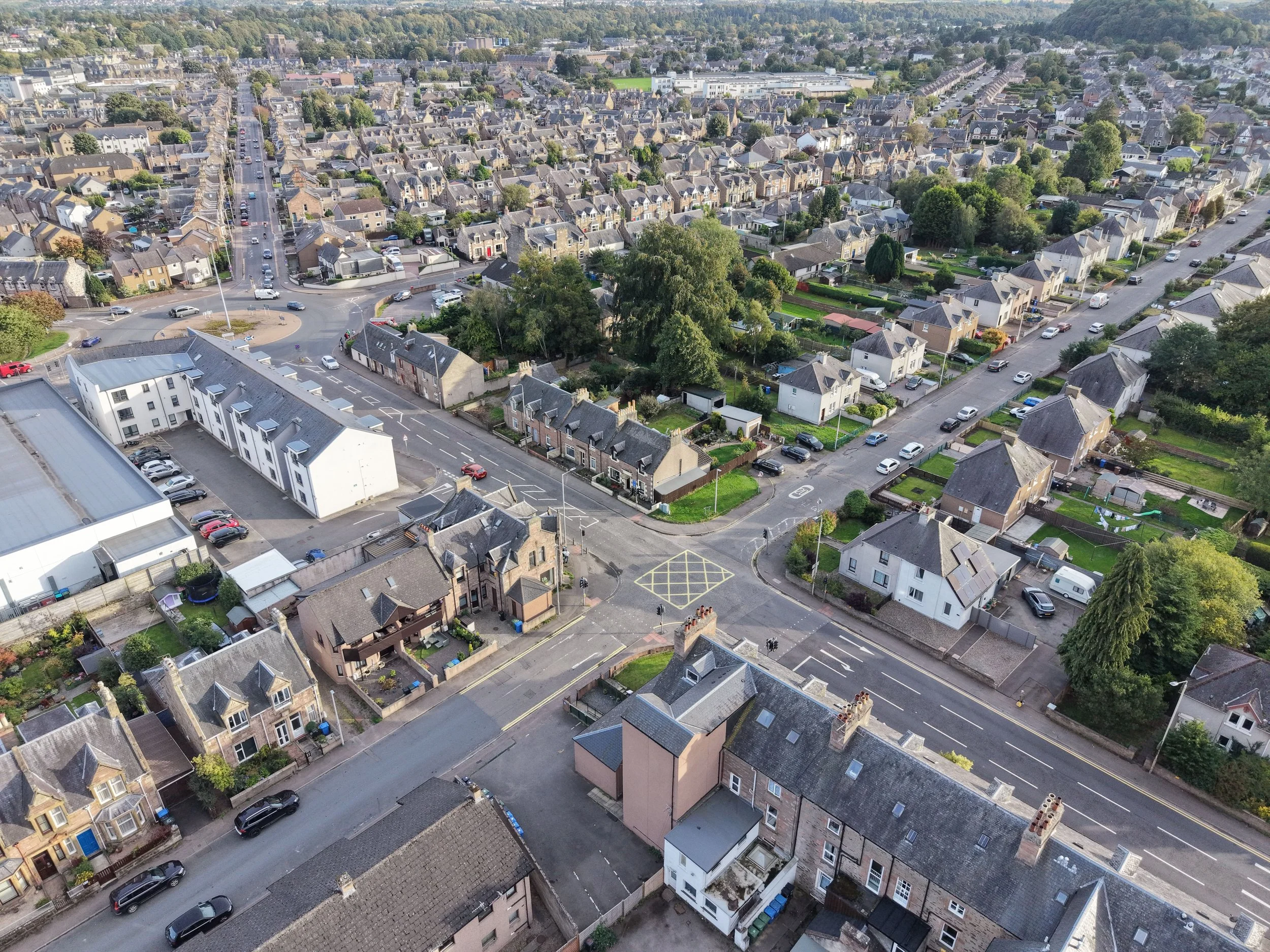 An aerial view of a residential neighborhood in a small town, showing houses, streets, trees, and parked cars.